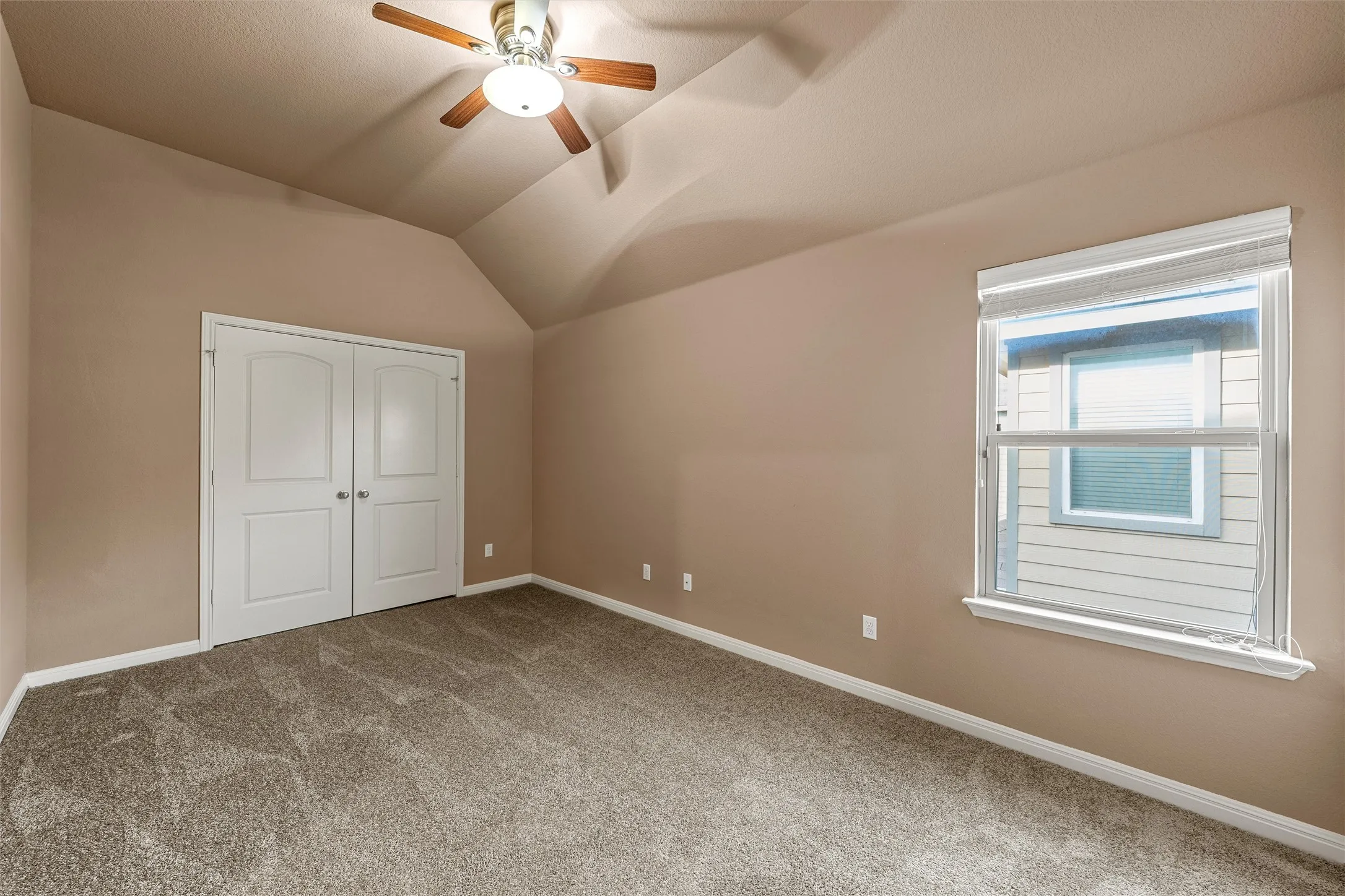 Vaulted ceiling with an attached ceiling fan, neutral carpet flooring, and a double-door closet