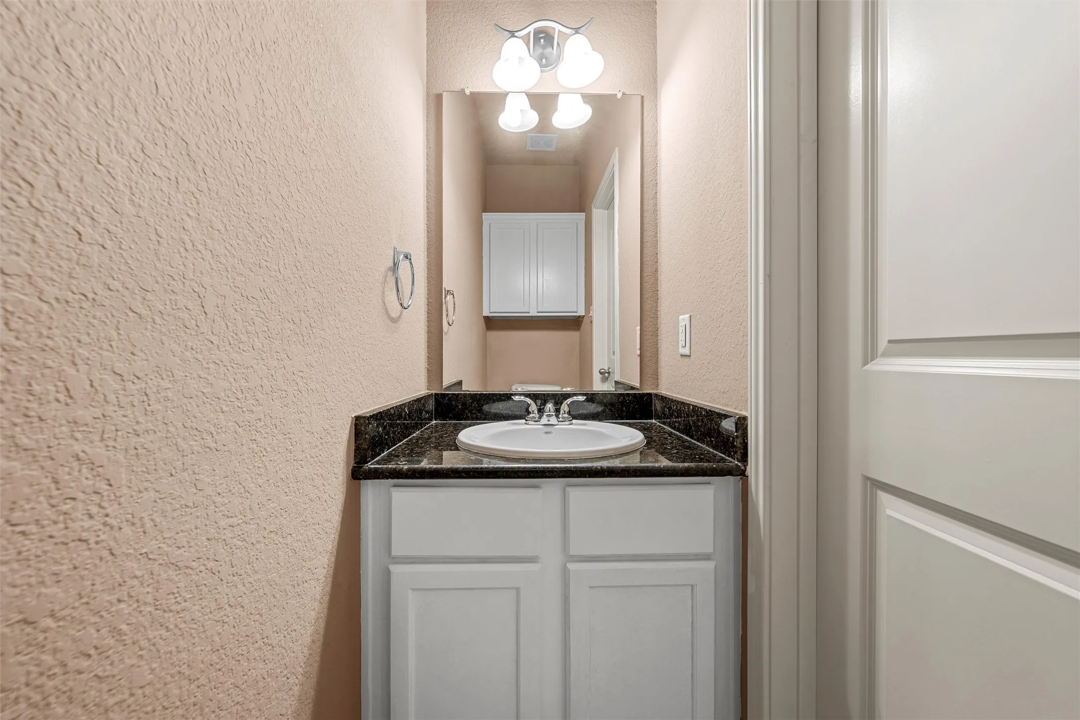 White vanity with an integrated sink, dark countertop, and sconce lighting