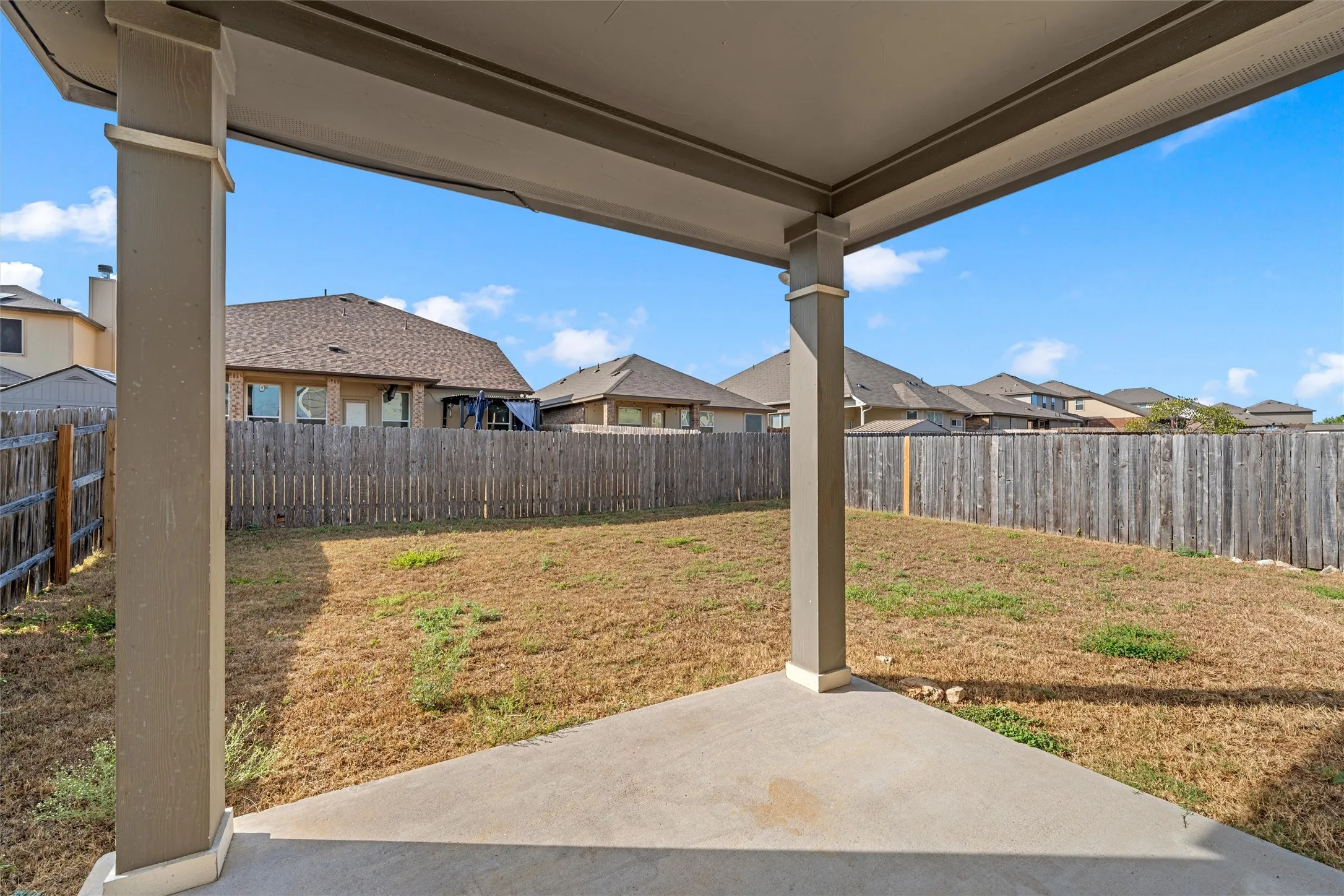 Covered patio with a concrete surface, wooden privacy fence, and expansive backyard