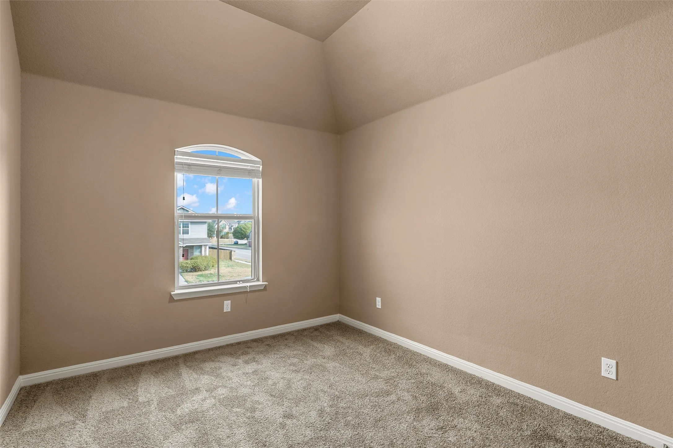 Vaulted ceiling with an arched window, neutral-toned walls, and plush carpeting