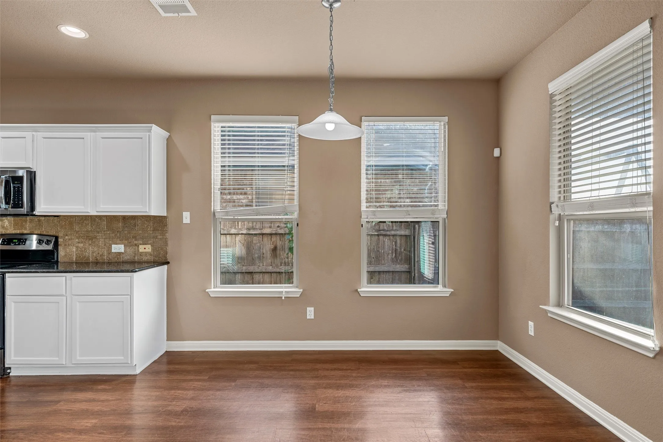 Wood-finish flooring, white cabinetry, dark countertops, and a tiled backsplash