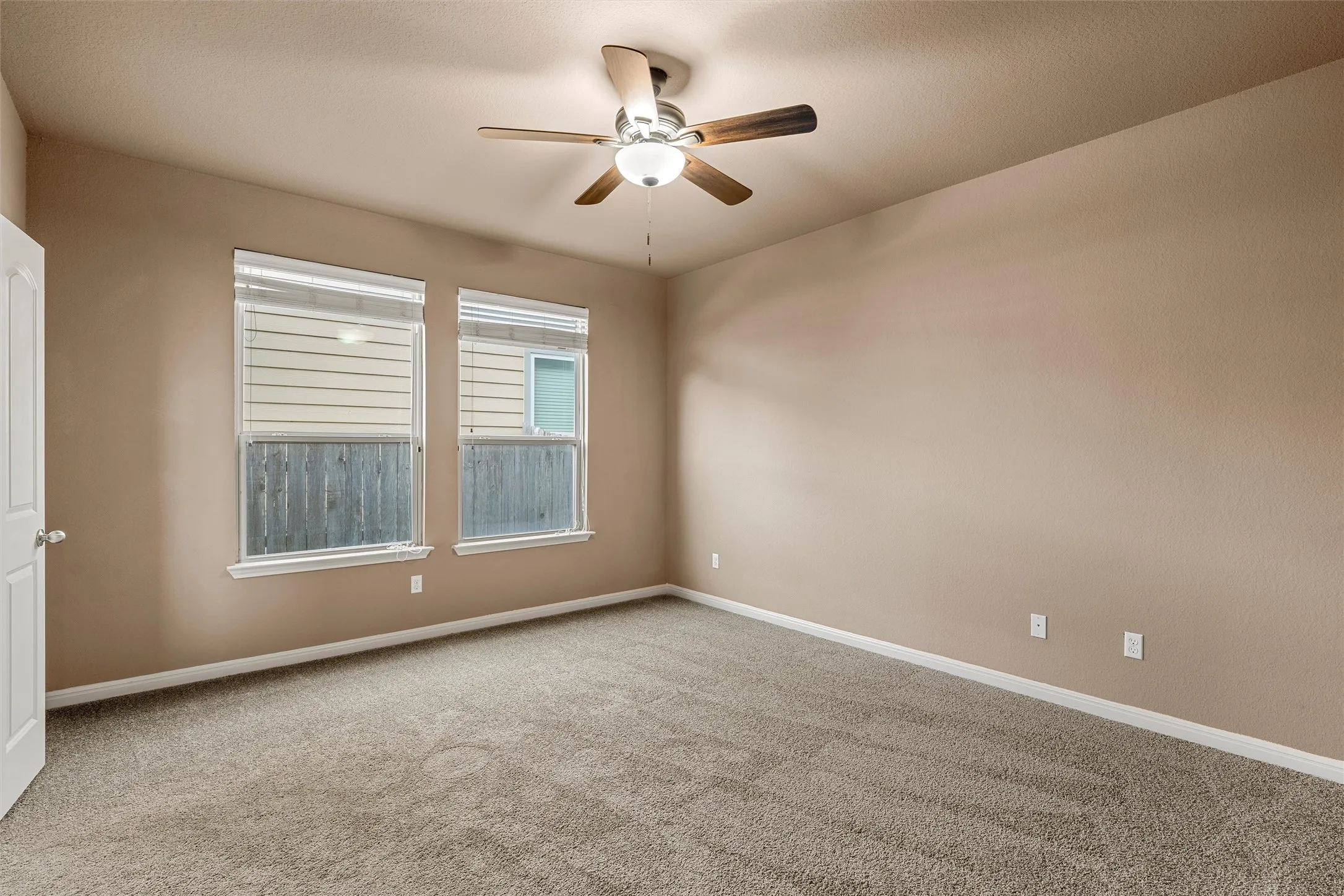 Vaulted ceiling with a ceiling fan, dual windows with blinds, and neutral carpeting