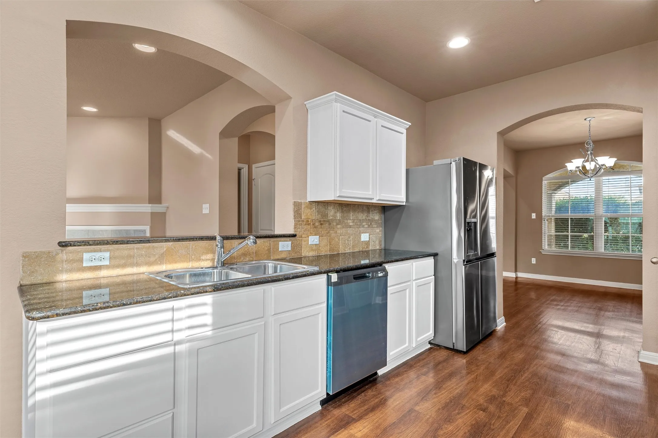 Kitchen featuring white cabinetry, granite-style countertops, dual basin sink, and stainless steel appliances