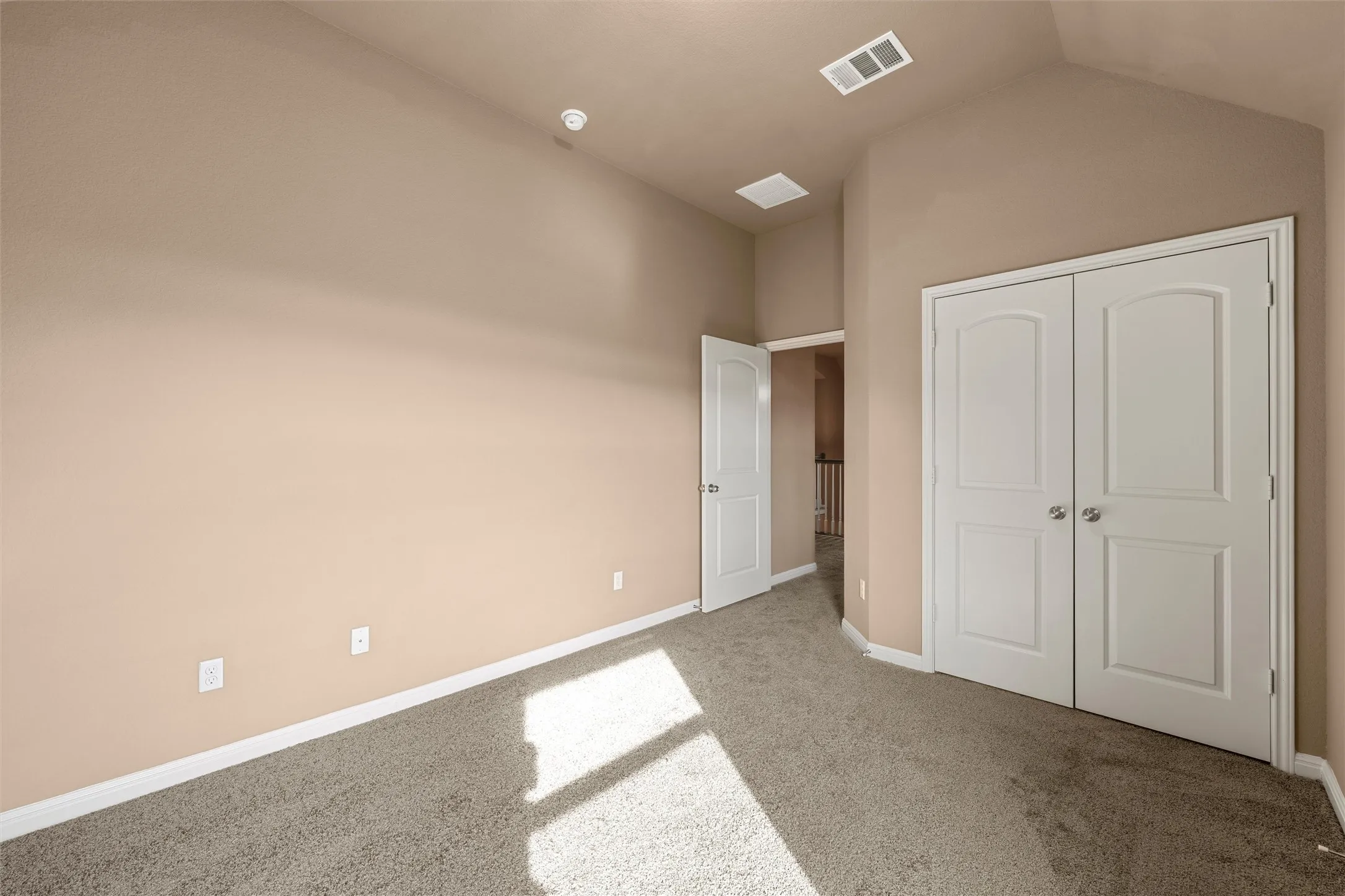 Vaulted ceiling, neutral wall tones, carpet flooring, white trim, and white bi-fold closet doors