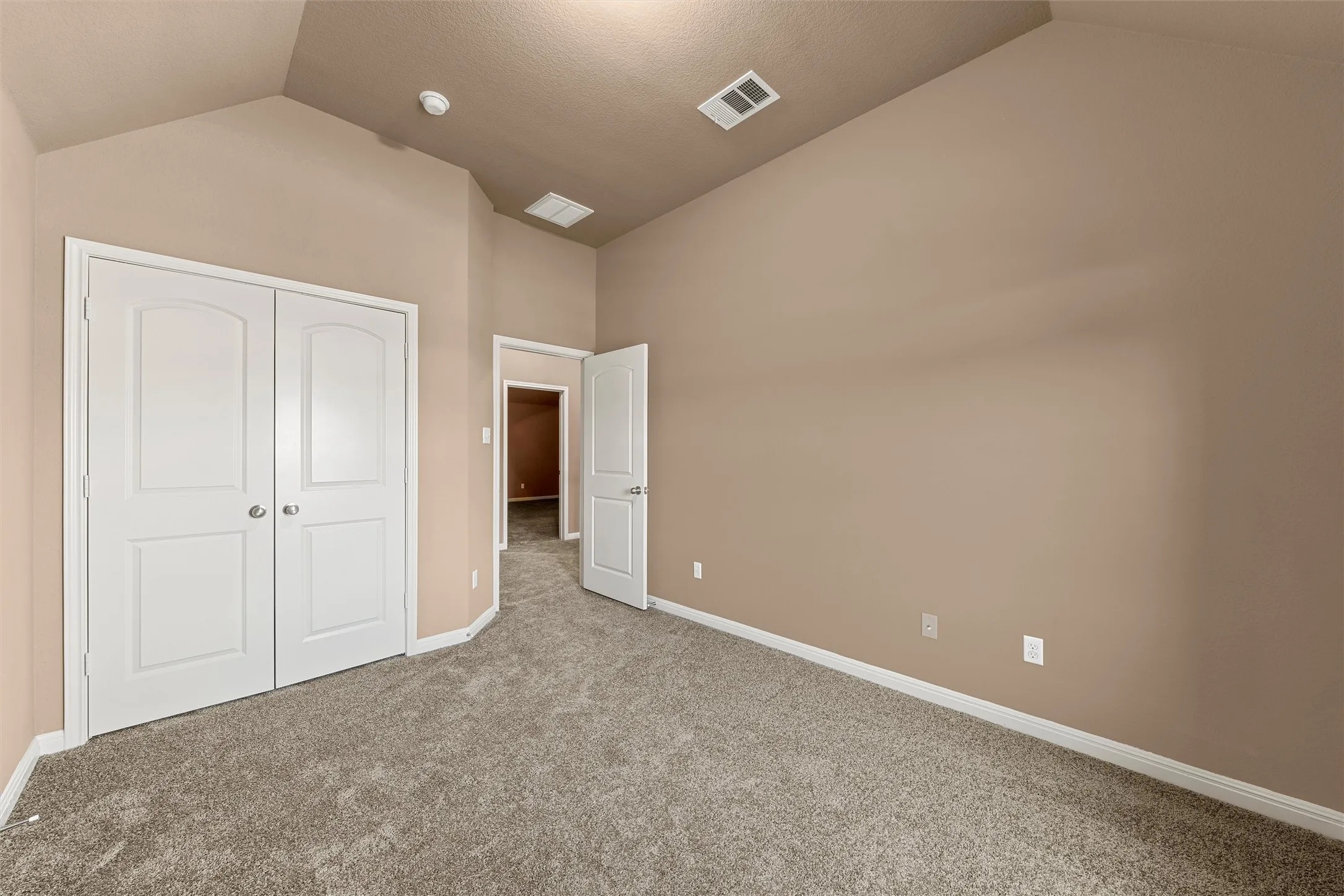 Vaulted ceiling with textured finish, neutral paint, plush carpet flooring, and white paneled doors