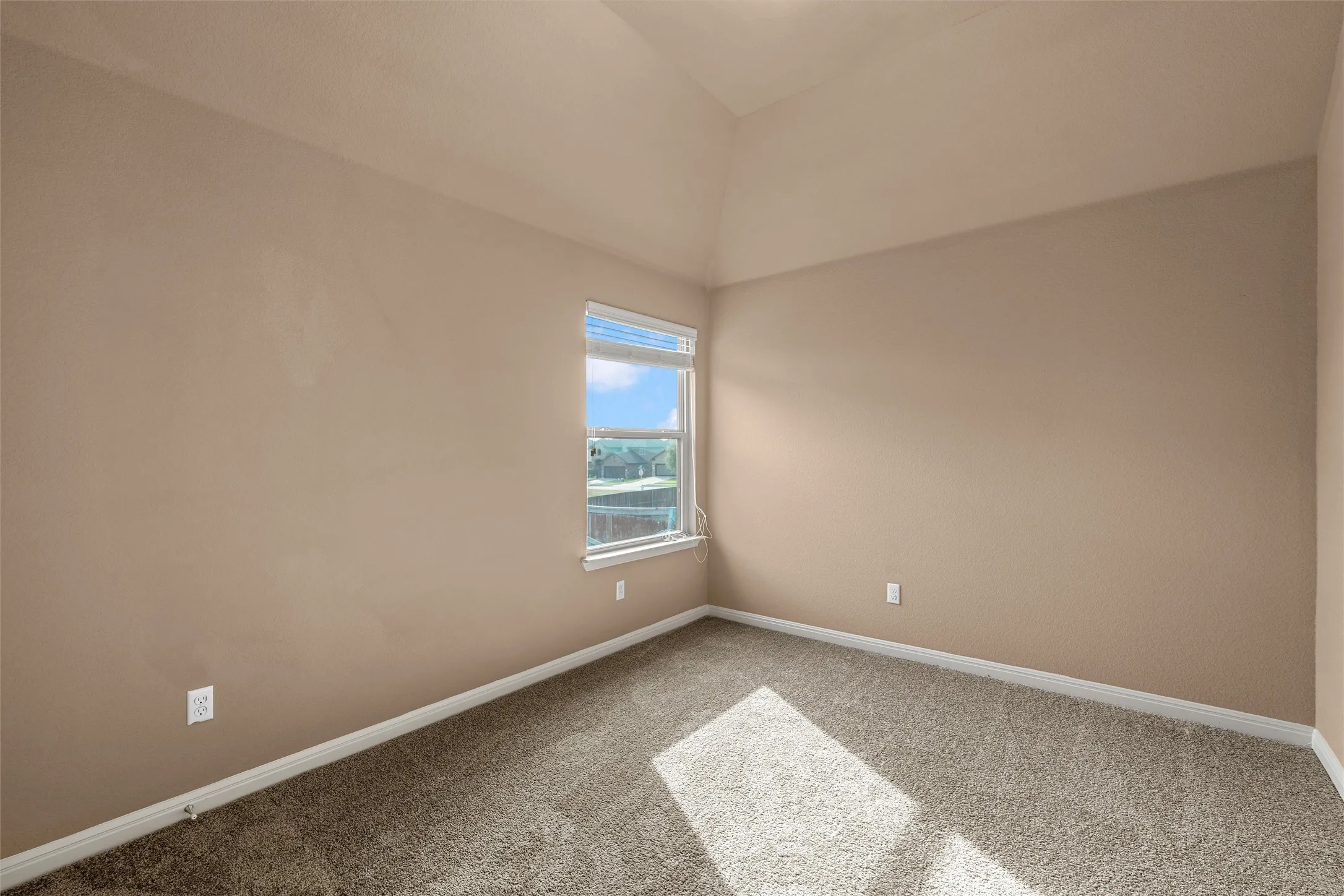 Vaulted ceiling with textured walls, carpet flooring, and a single window with blinds