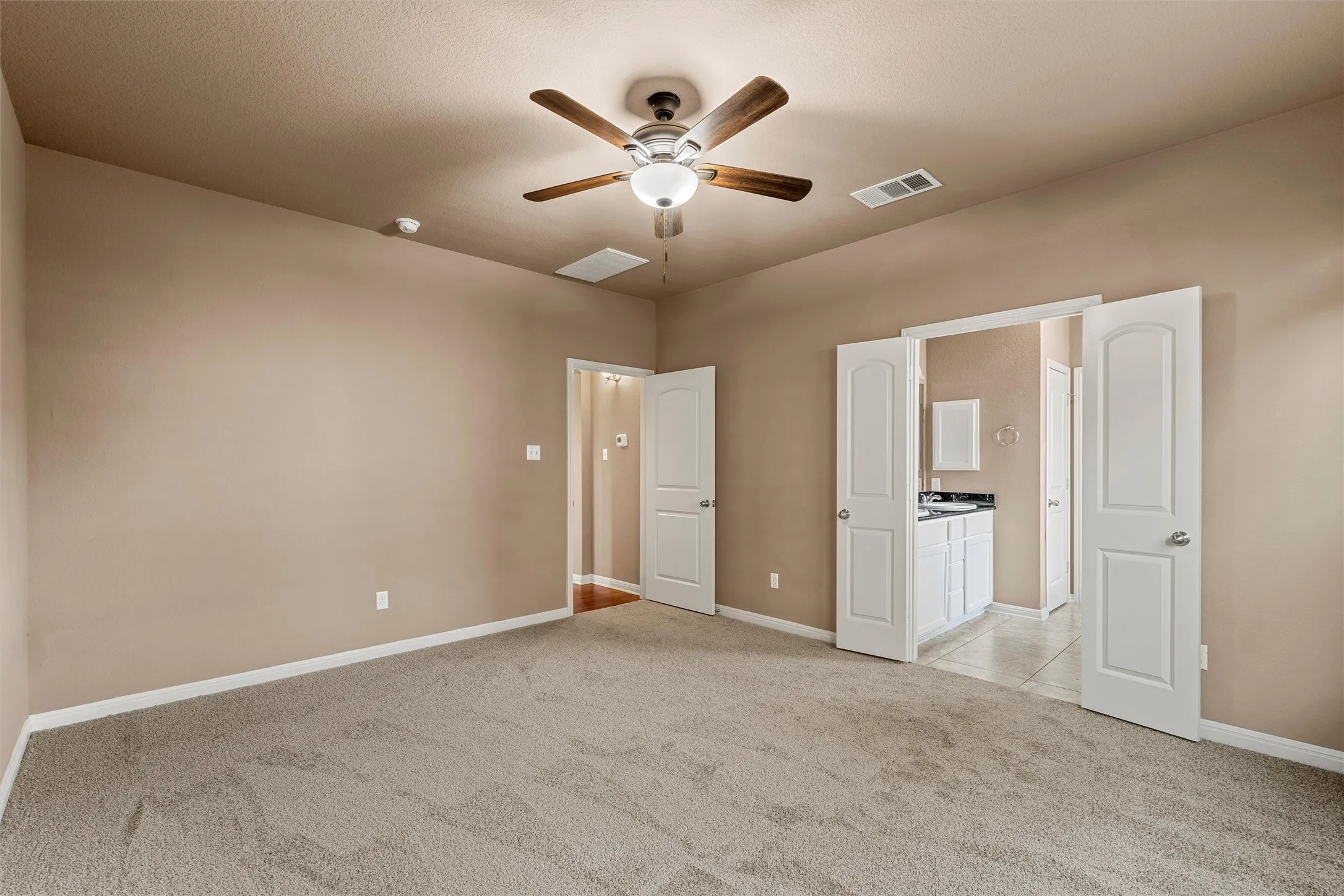 Carpeted flooring, vaulted ceiling, ceiling fan with integrated lighting, white paneled doors, and an en-suite bathroom featuring a vanity with dark countertop and white cabinetry