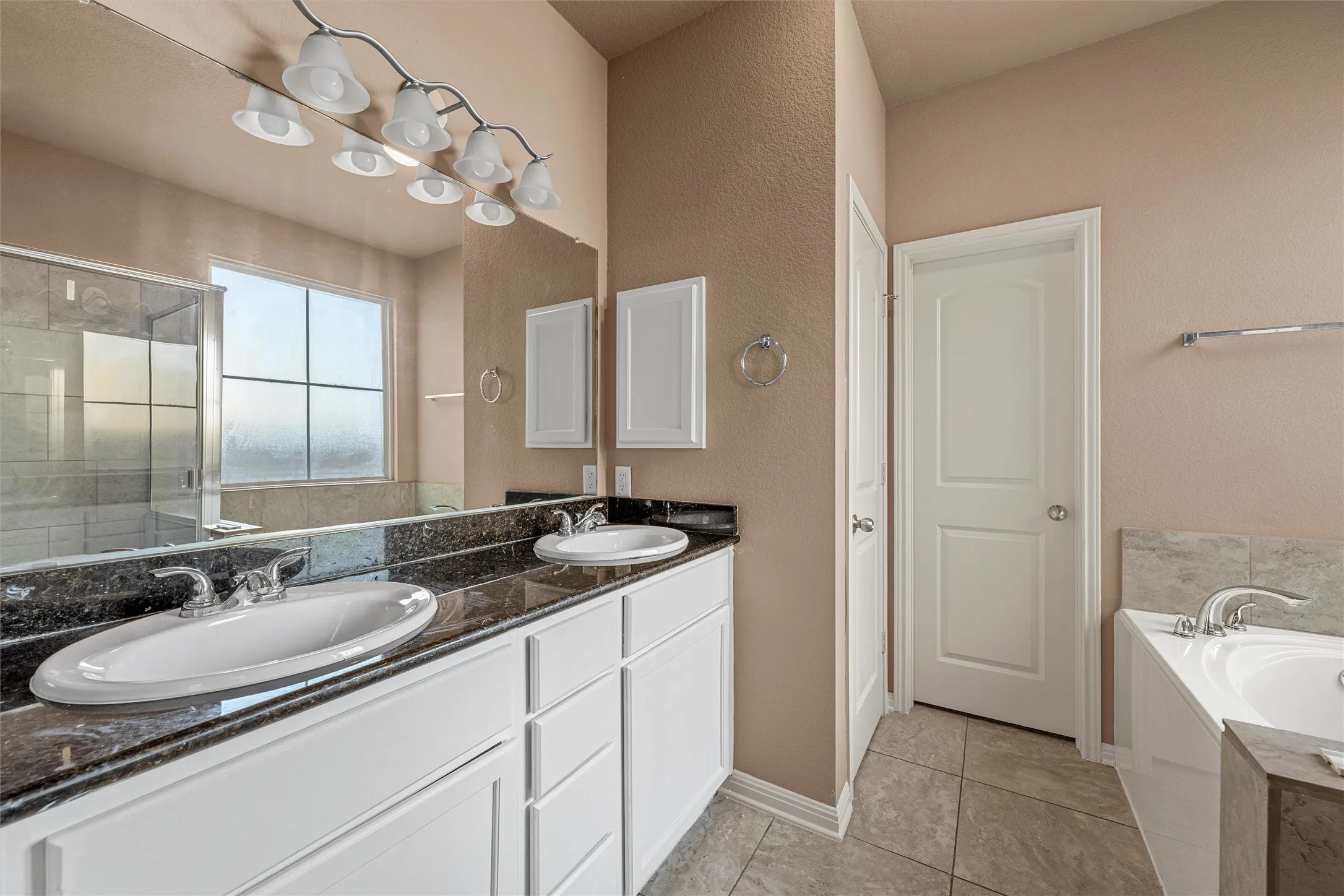 Bathroom featuring a dual vanity with undermount sinks, a dark countertop, white cabinetry, and a built-in bathtub