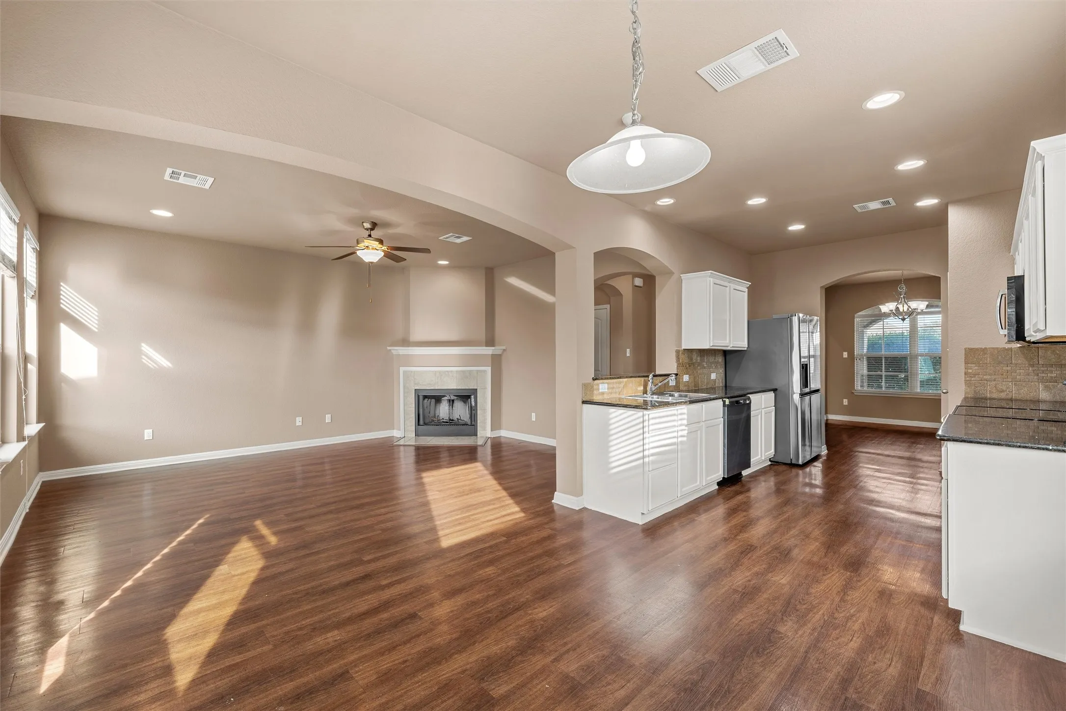 Open concept interior featuring wood-finish flooring, a fireplace with a stone surround, recessed lighting, and a kitchen island with built-in appliances