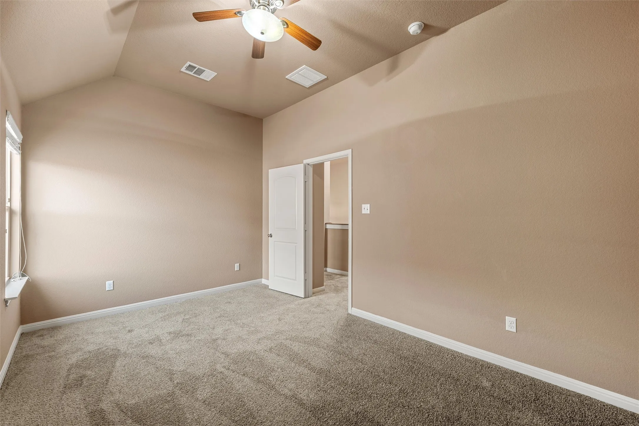 Vaulted ceiling with a ceiling fan, carpeted flooring, and a window for natural light