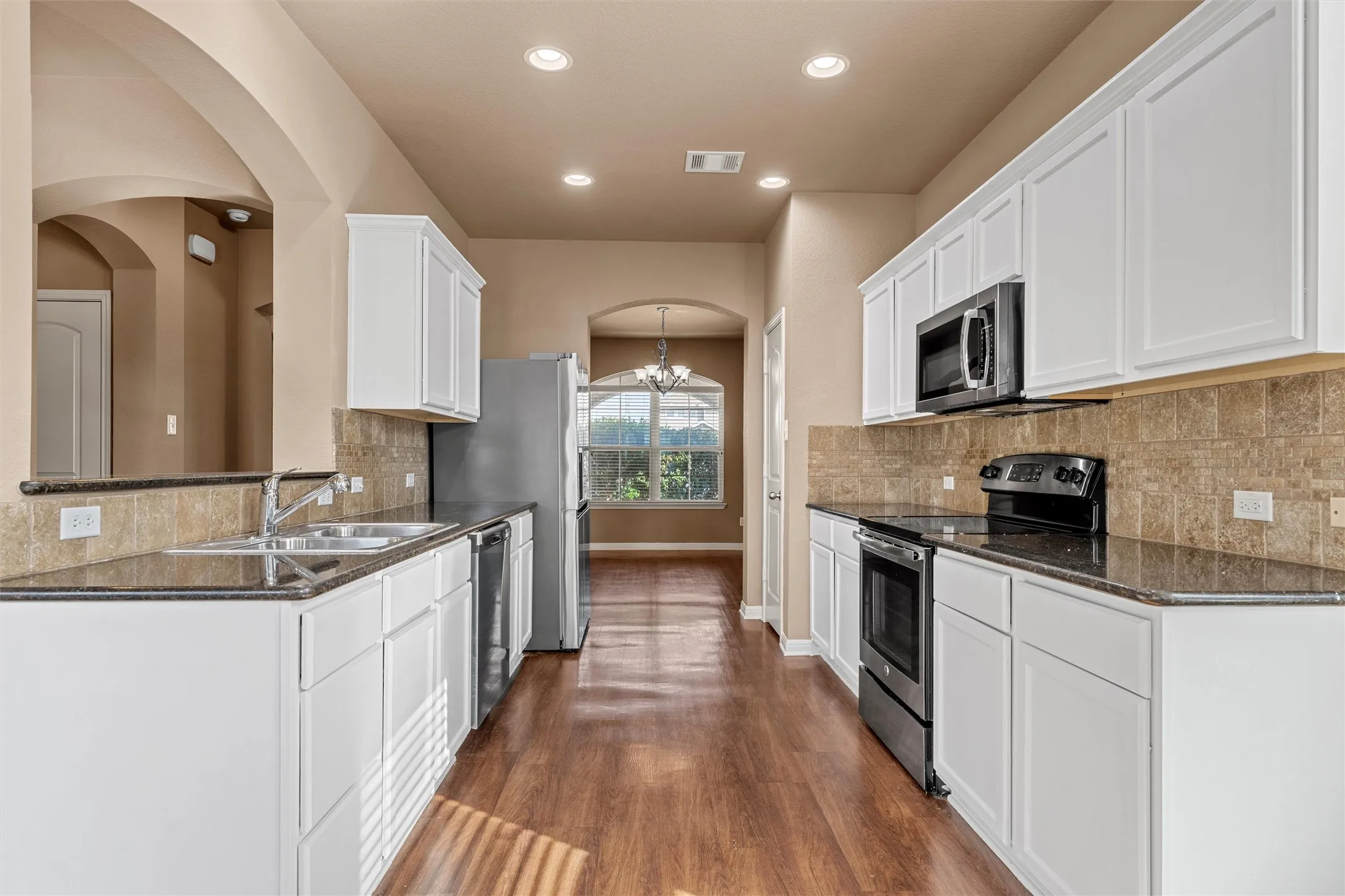 Kitchen featuring white cabinetry, dark countertops, built-in stainless steel appliances, a tiled backsplash, and wood-finish flooring