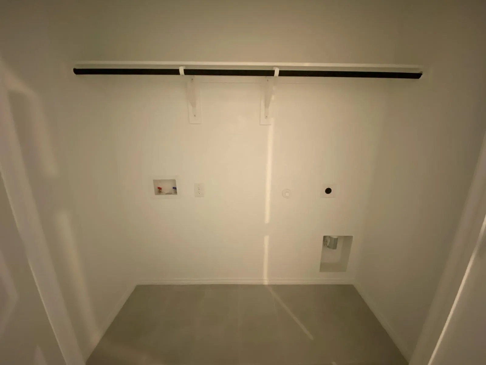 Laundry area with overhead hanging rod and utility hookups