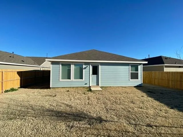 Light blue siding exterior with a dark shingle roof, featuring multiple window openings and a private backyard enclosed by wood fencing