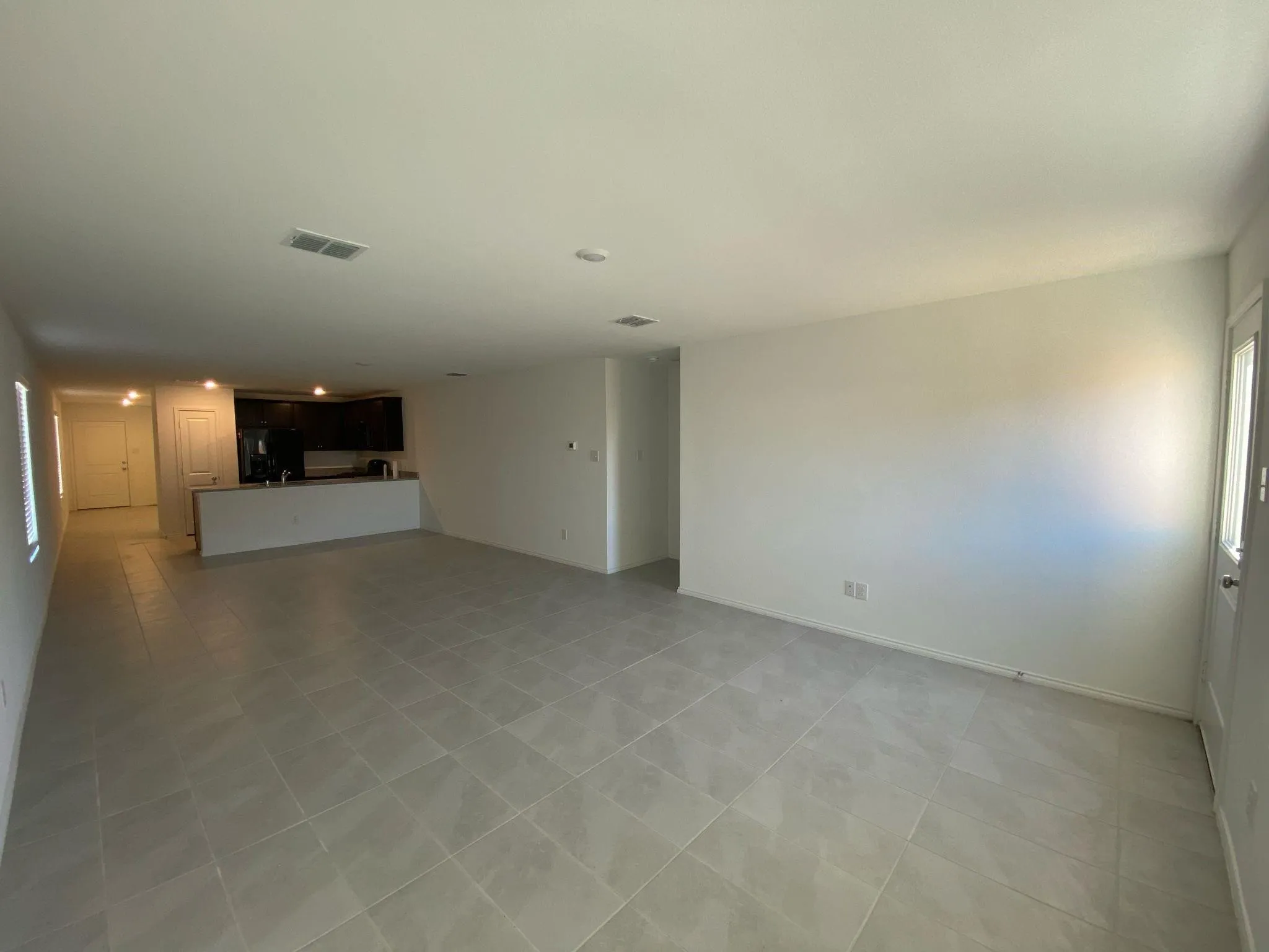 Open-concept living area featuring tile flooring, white walls, recessed lighting, and a kitchen pass-through with dark cabinetry