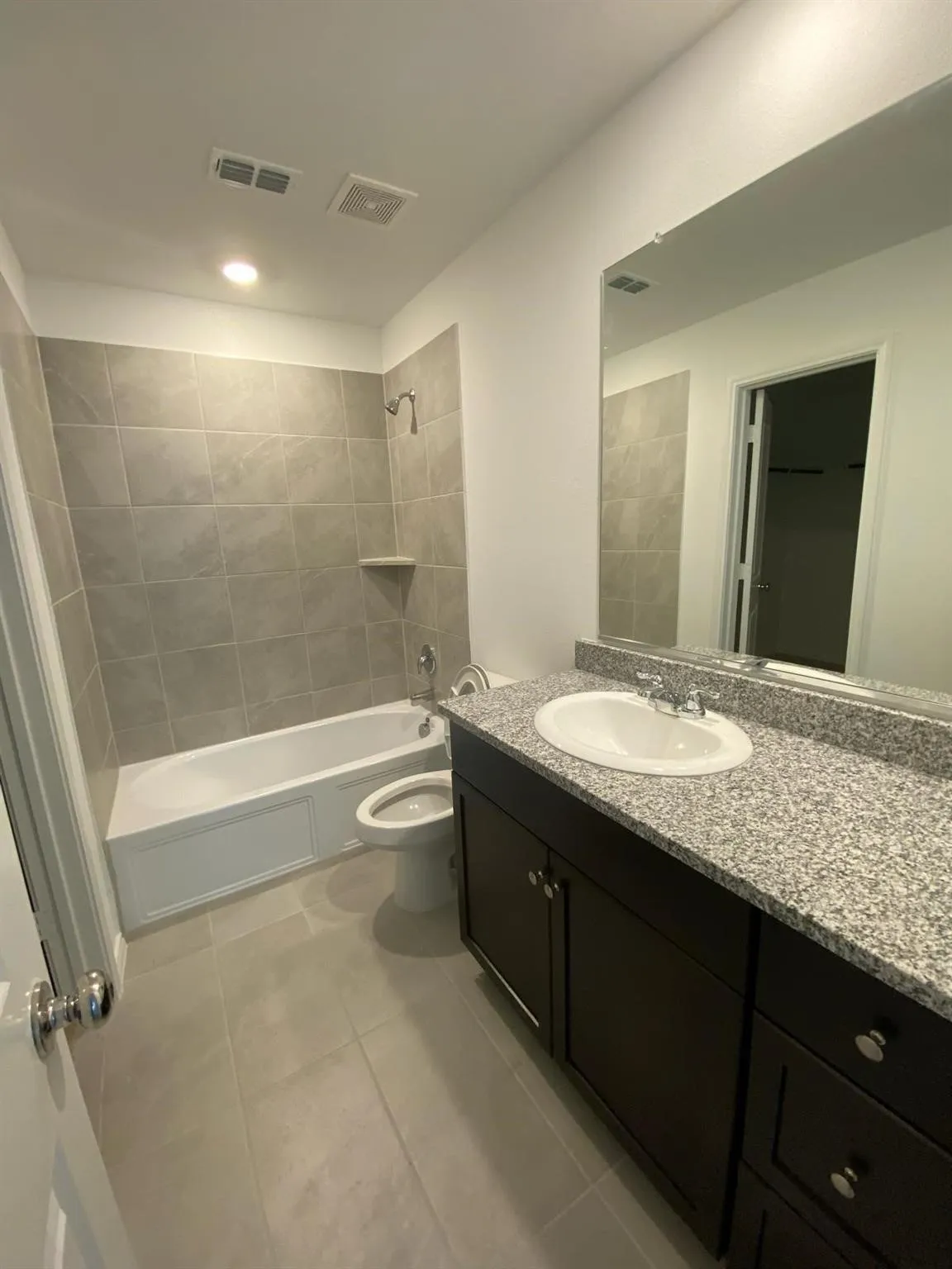 Bathroom featuring a bathtub with tiled surround, a built-in shower niche, a vanity with granite-finish countertop, and a large wall-mounted mirror