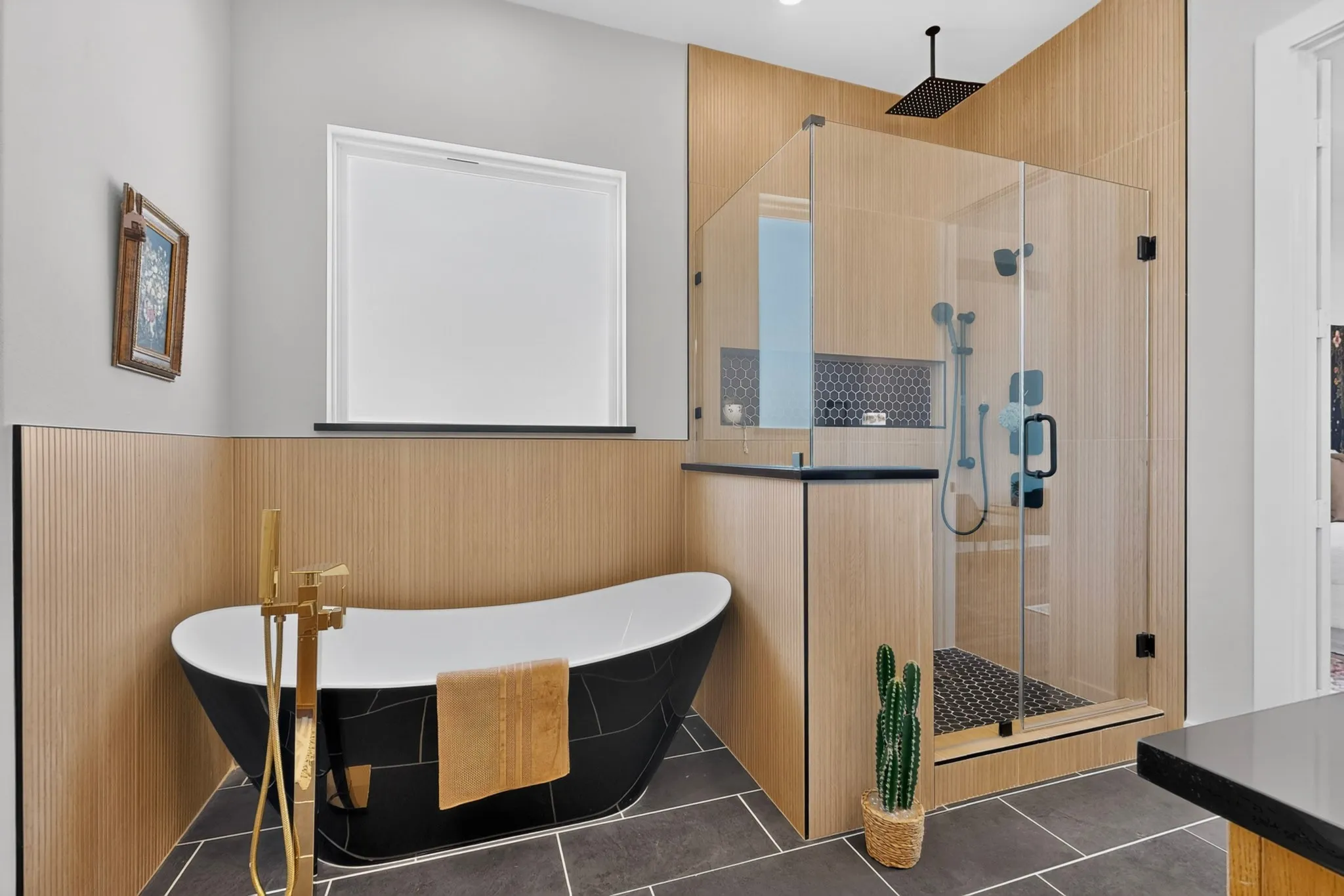 Freestanding black soaking tub with gold-finish floor-mounted faucet, glass-enclosed shower with black-finish fixtures and wood-paneled walls