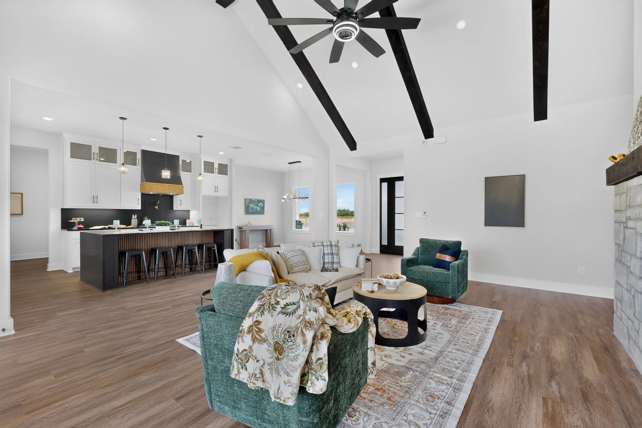 Open-concept living area featuring wood-finish flooring, a vaulted ceiling with exposed beams, and a stone-faced fireplace with a wood mantel