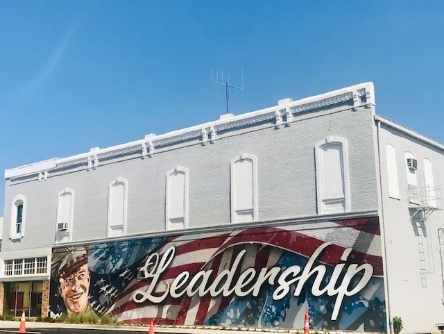 Brick exterior with decorative cornice detailing, prominent mural artwork, ground-level commercial windows, and a side fire escape