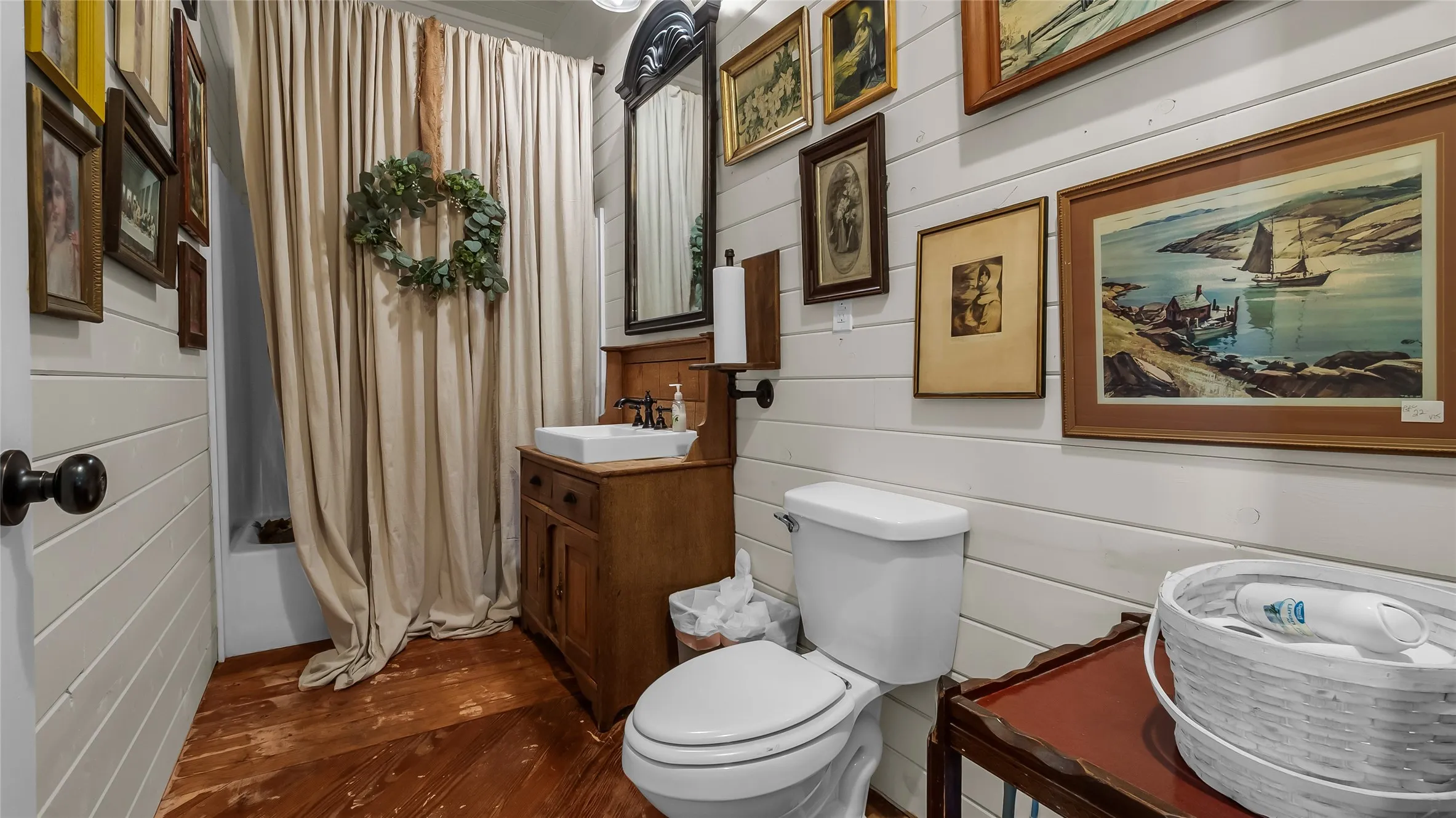 Shiplap wall paneling, wood-finish flooring, and a pedestal sink with a framed mirror