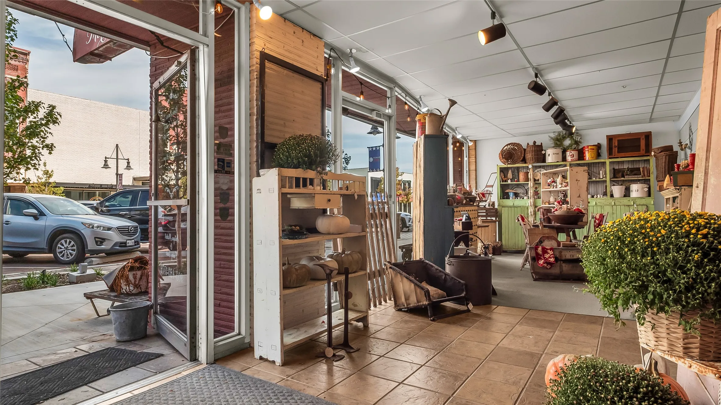 Glass storefront with an open entrance, track lighting, exposed brick accents, and tiled flooring