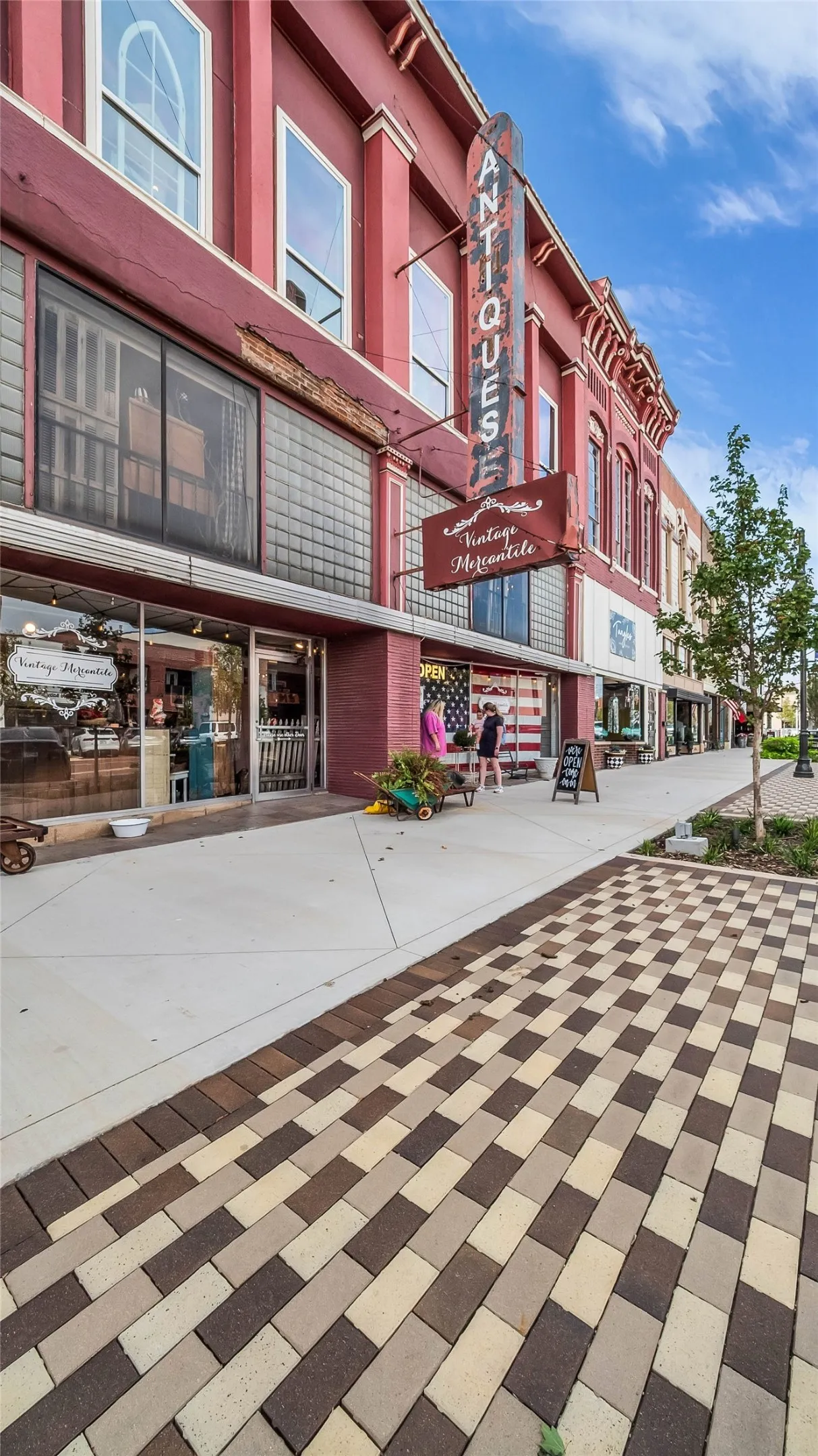 Red brick facade with arched windows, prominent commercial signage, glass block window, and a patterned paver sidewalk