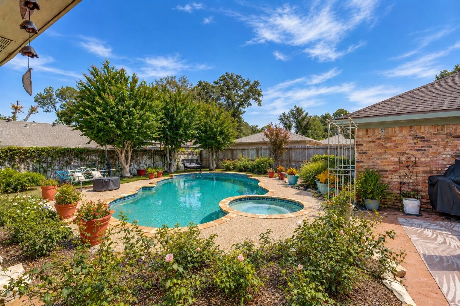 Resort-style backyard featuring a freeform swimming pool, integrated spa, and extensive hardscaping with mature landscaping