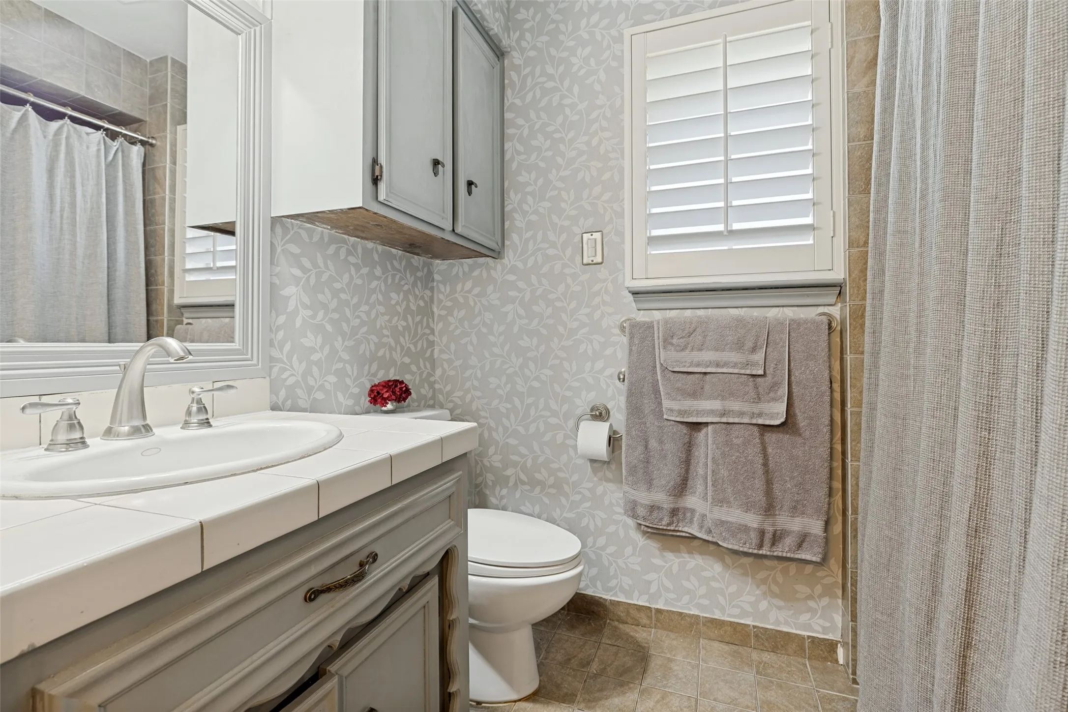 Vanity with white tiled countertop, brushed nickel faucet, framed mirror, and upper storage cabinetry