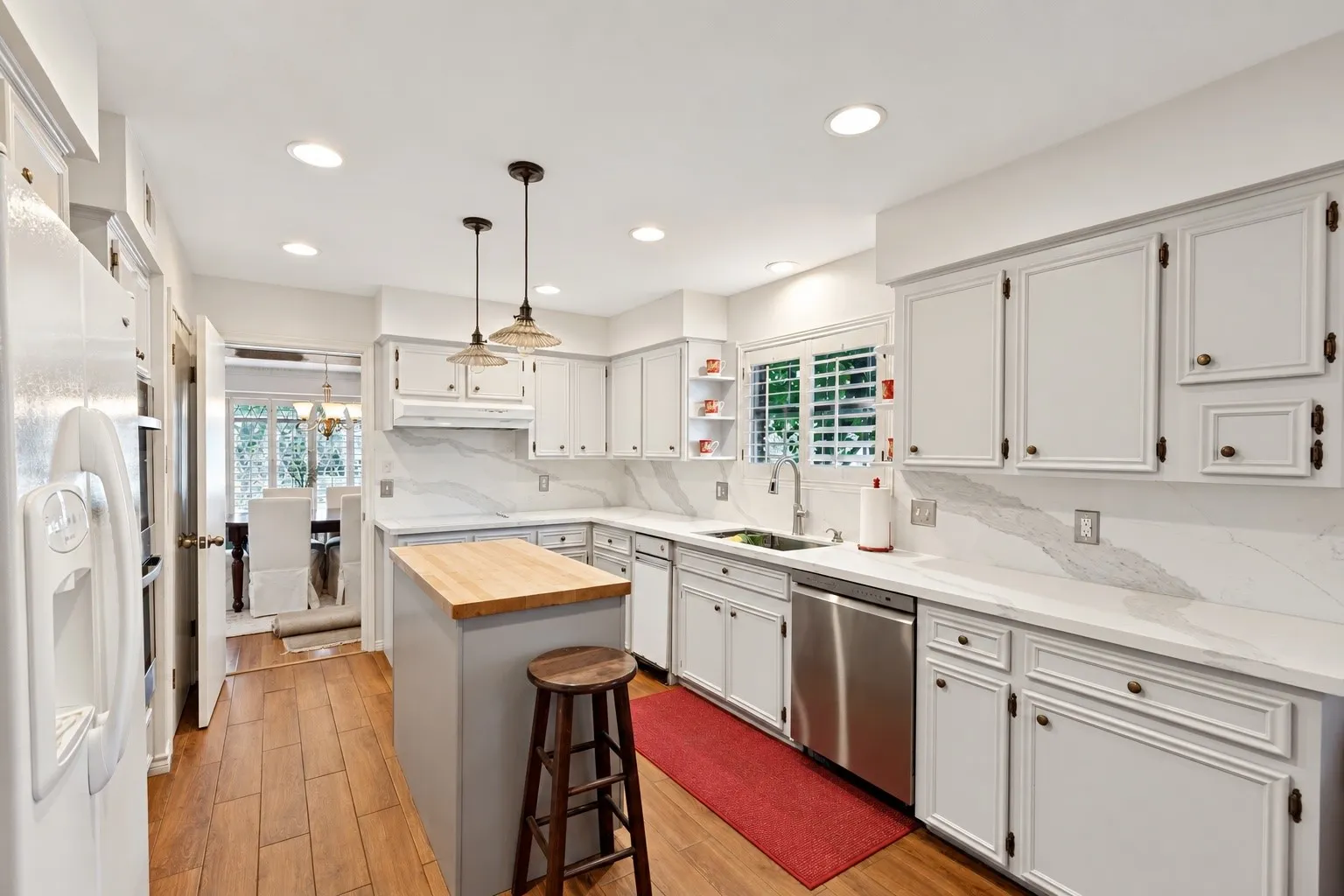 Kitchen featuring white cabinetry, light-toned countertops with matching backsplash, wood-finish flooring, a central island with a wood butcher-block top, and stainless steel appliances