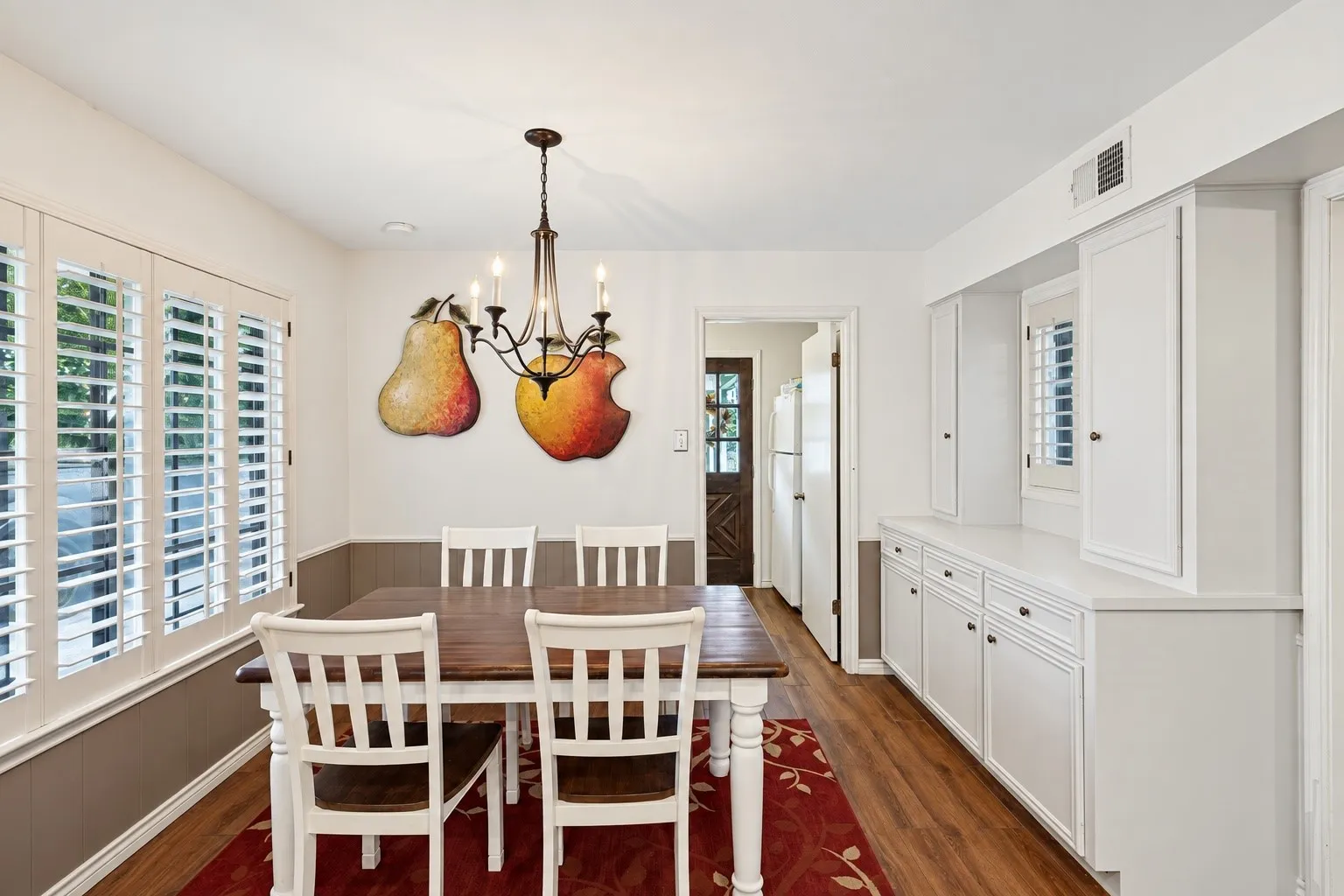Wood-finish flooring, white plantation shutters, built-in white cabinetry with a light-colored countertop, and a classic chandelier