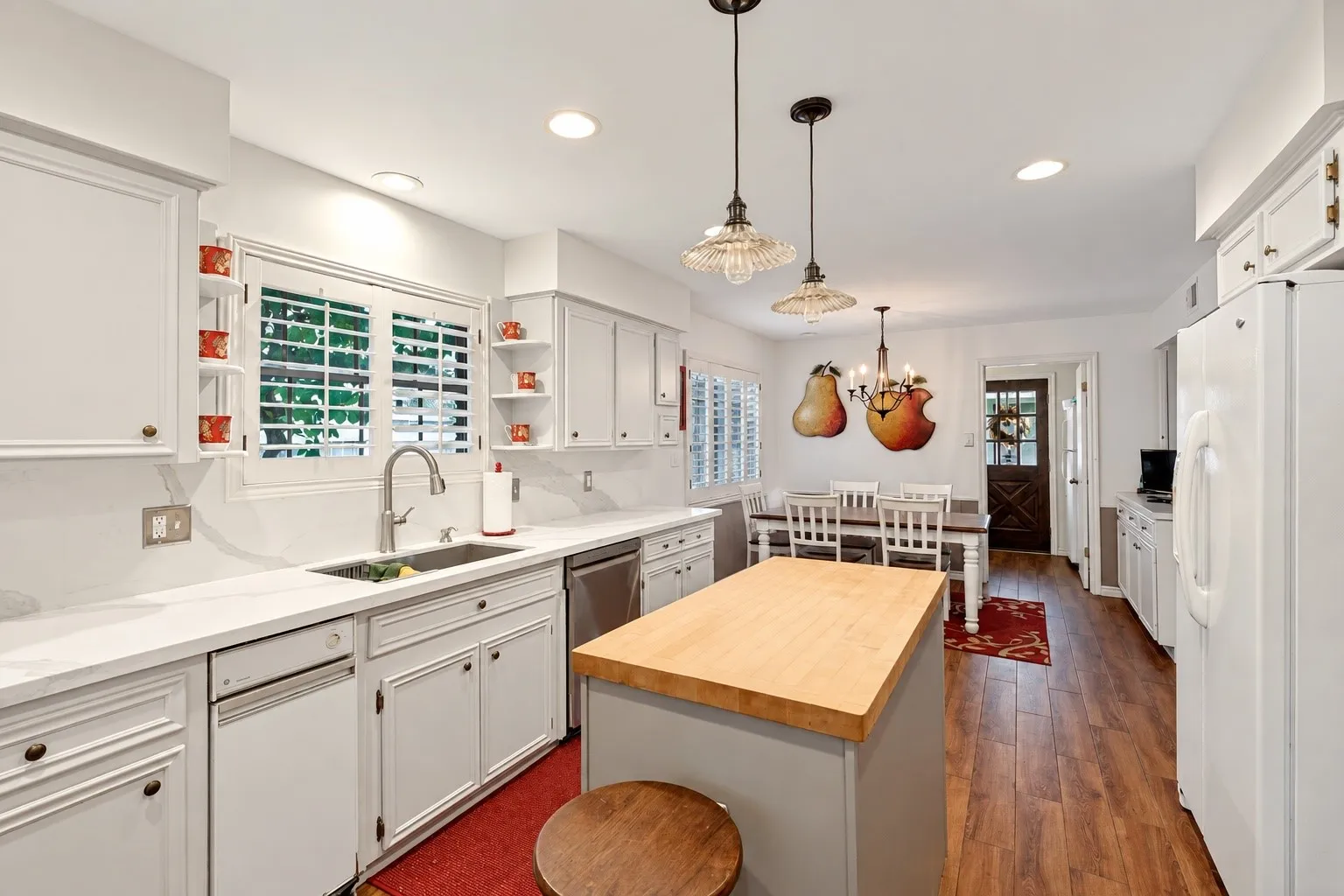 White cabinetry with brushed nickel hardware, light-toned countertops, stainless steel sink with gooseneck faucet, wood-finish flooring, and a kitchen island with a butcher block top