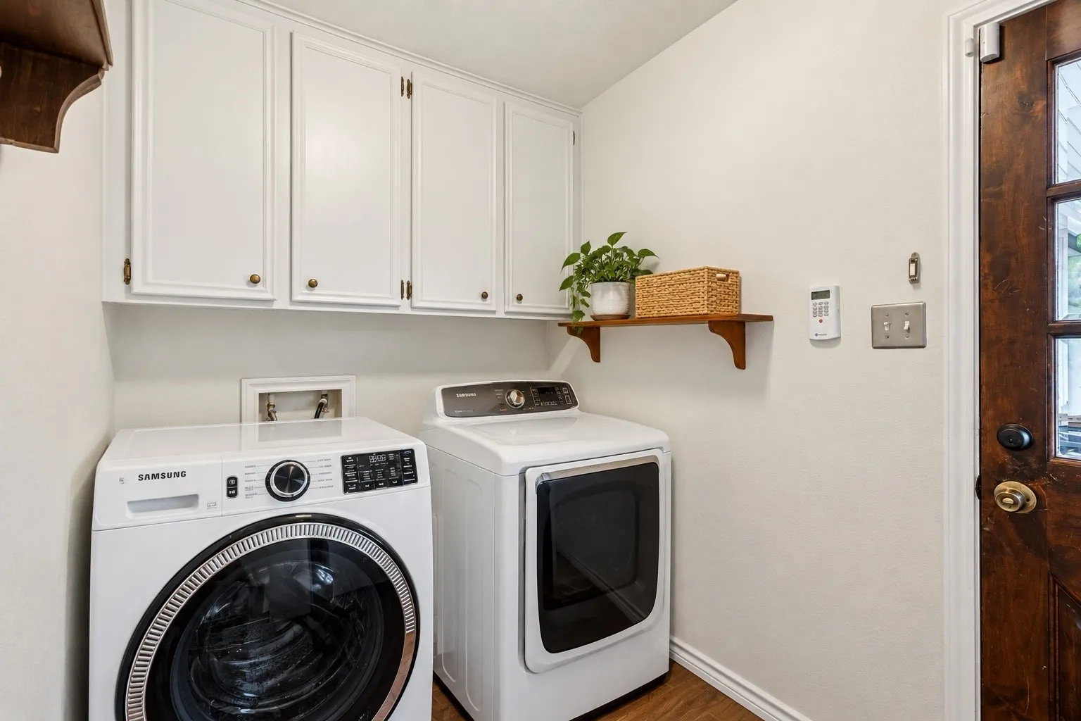 Wood-finish flooring, white overhead cabinetry with brass hardware, and a stained wood door with glass inserts