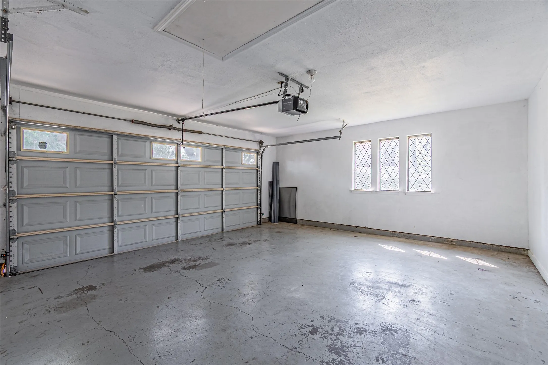 Attached two-car garage featuring a panel door with transom windows, three diamond-paned windows, and a concrete floor