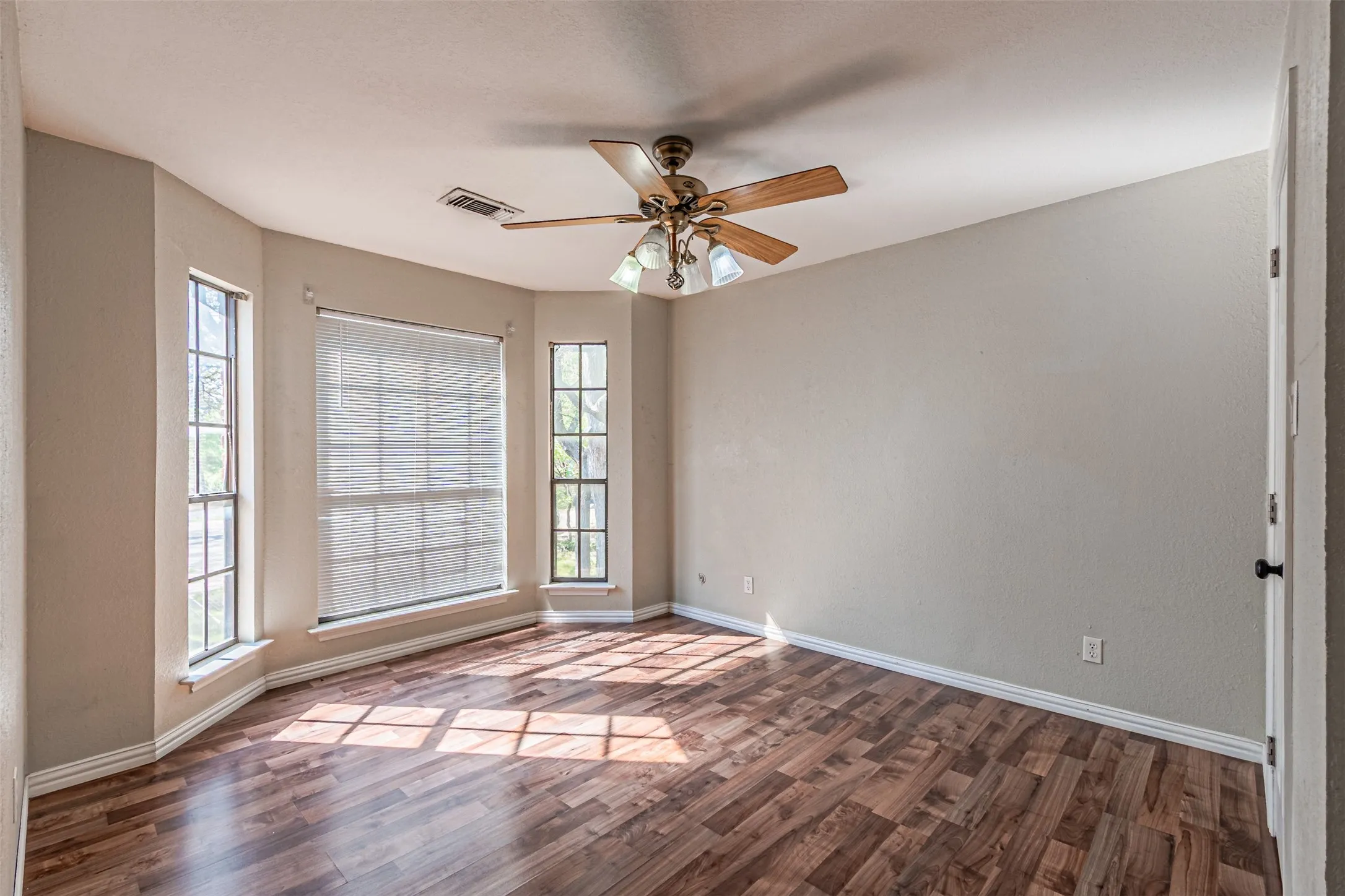 Wood-finish flooring throughout, ceiling fan with integrated lighting, and multiple windows with roller shades