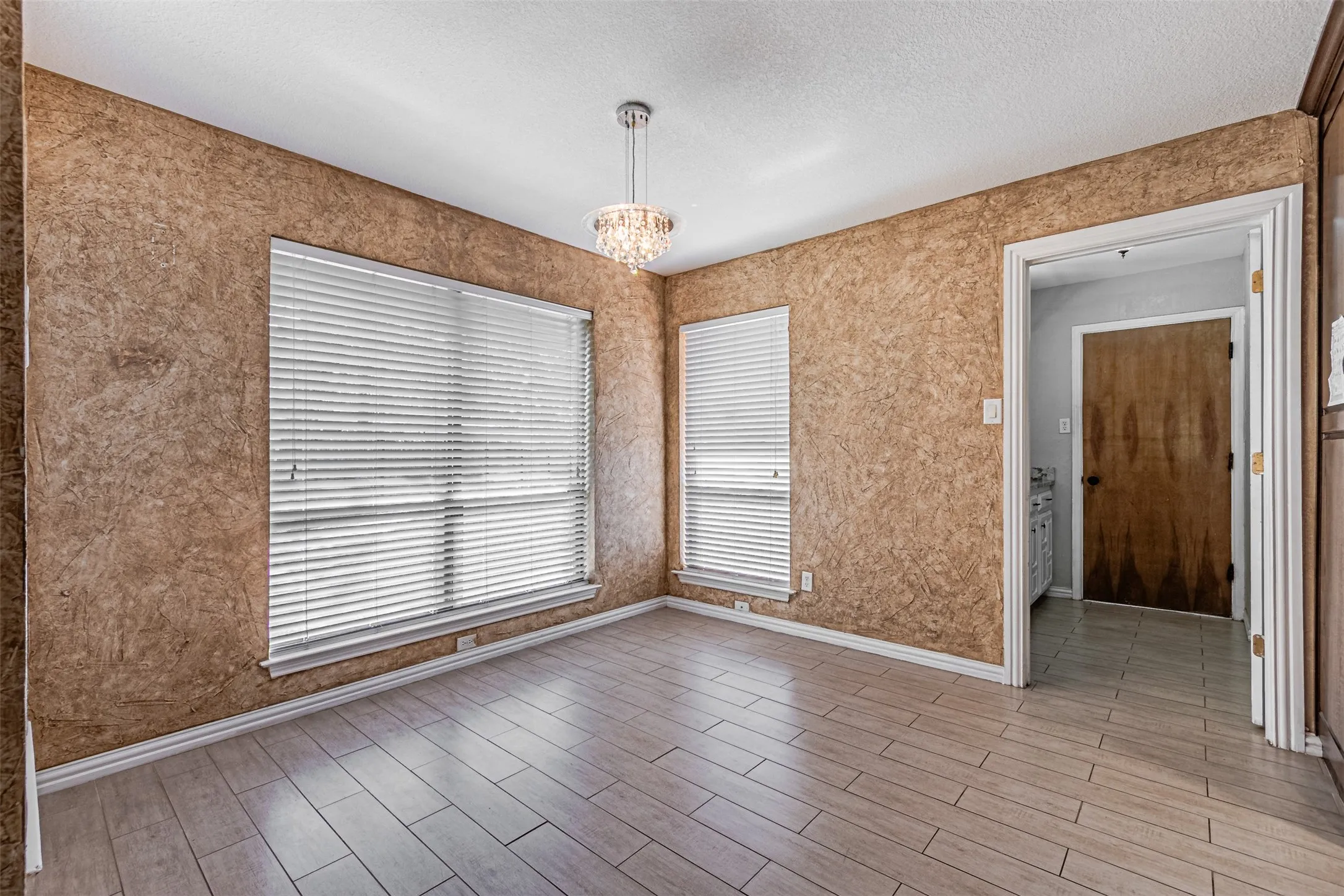 Wood-finish flooring with a crystal chandelier, textured wall finish, and white window blinds