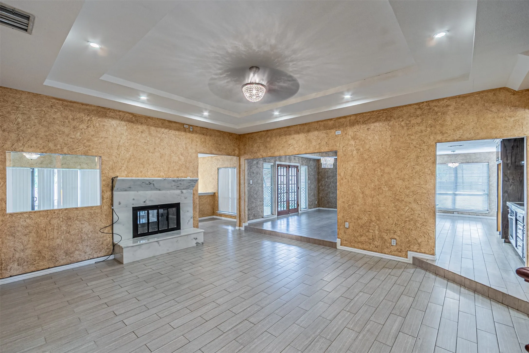 Recessed ceiling lighting, decorative ceiling fixture, tiled flooring, built-in fireplace with a stone surround, and an open doorway