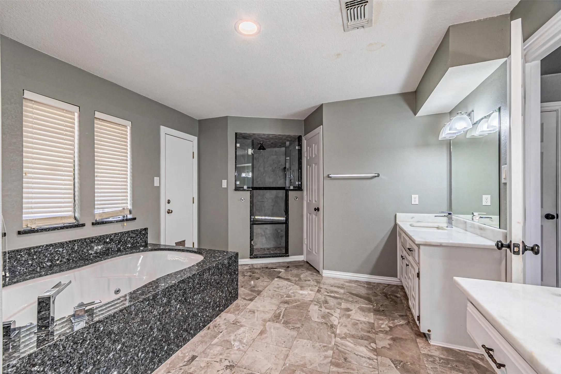 Soaking tub with a dark stone surround, walk-in shower with a glass enclosure, dual vanity with white countertops, and tiled flooring
