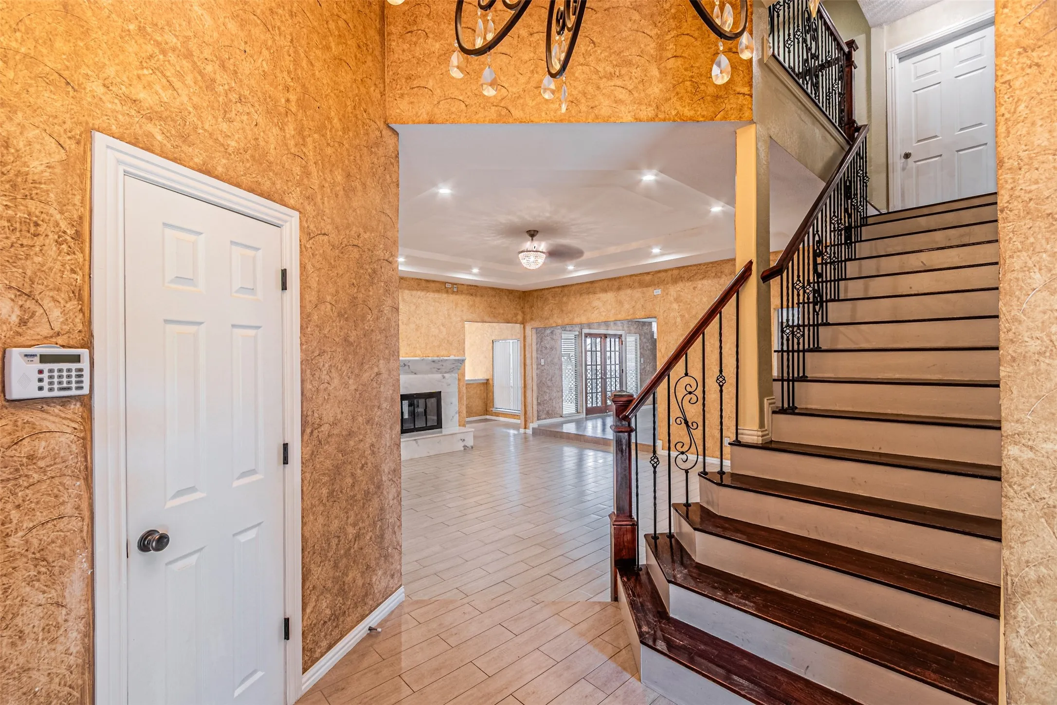 Ornate wrought iron railing, wood-finish stair treads, tile flooring, textured wall finish, and a fireplace with a light-colored surround