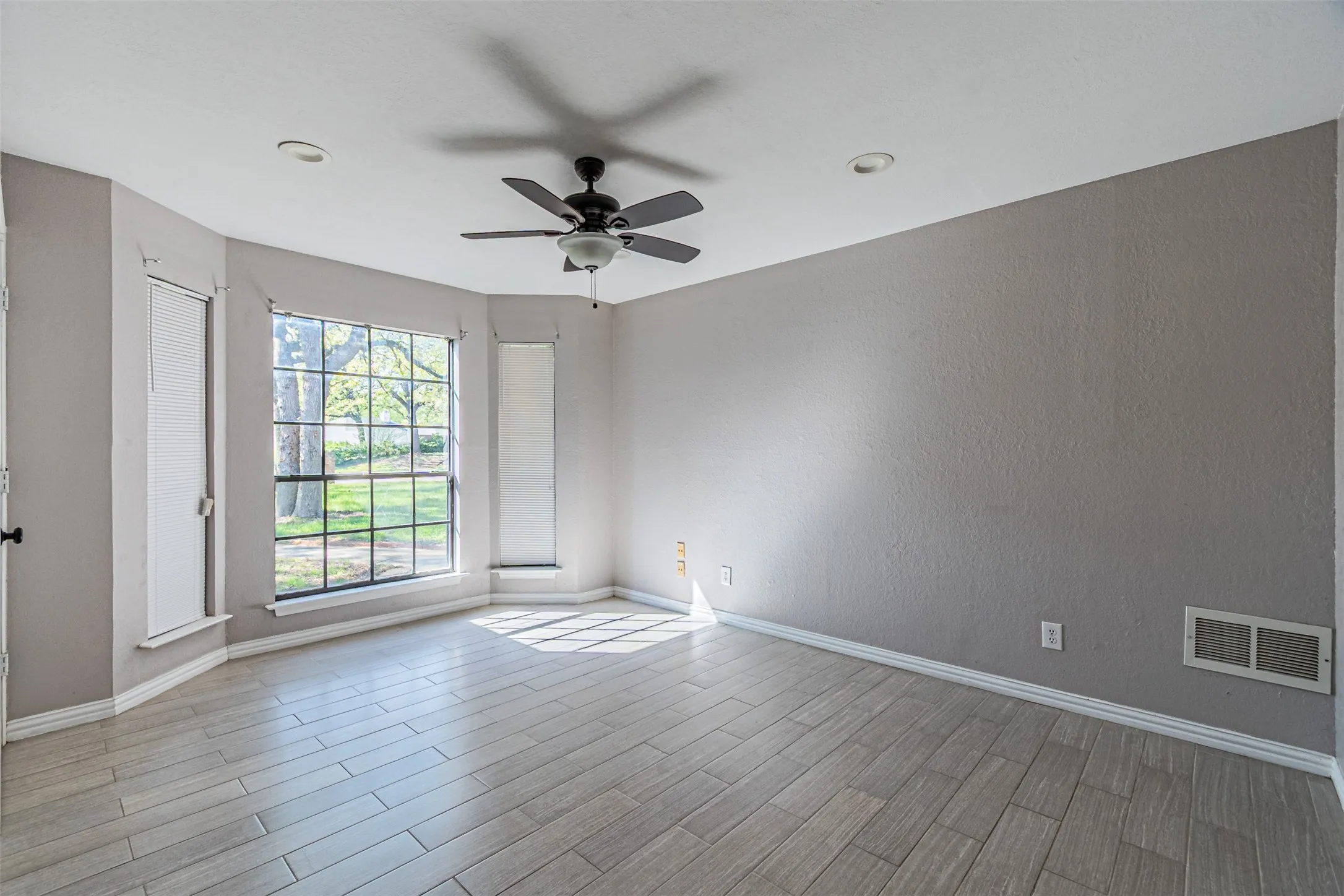 Wood-finish plank flooring, ceiling fan with integrated lighting, recessed ceiling lighting, and a bay window