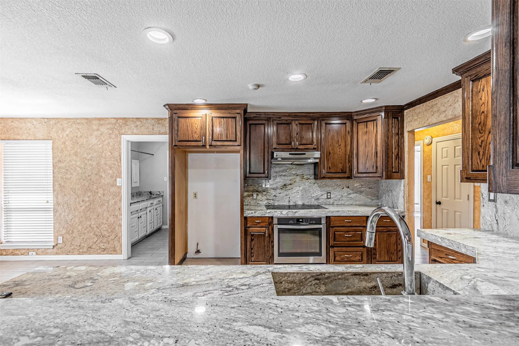 Kitchen featuring extensive cabinetry, stone countertops, a large single-basin sink with a high-arc faucet, and stainless steel appliances including a built-in oven and cooktop