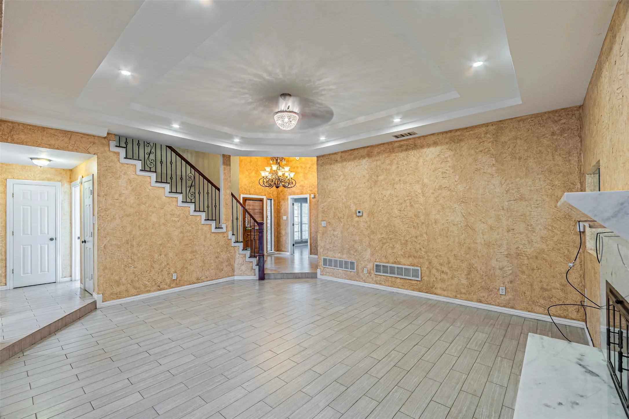 Recessed lighting, tray ceiling, tile flooring, wrought iron staircase railing, and a decorative chandelier