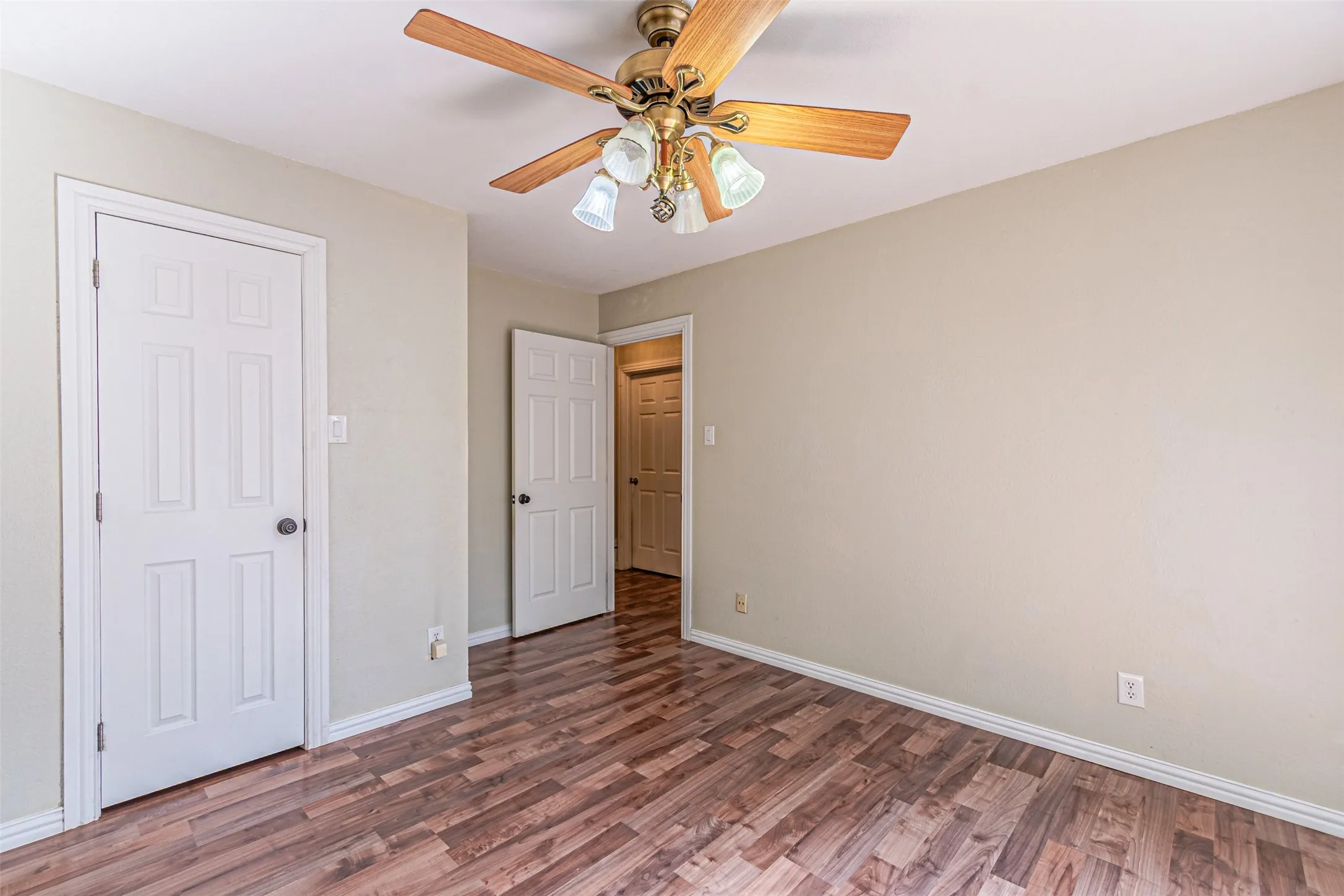 Wood-finish flooring, ceiling fan with integrated lighting, white trim, and white paneled doors