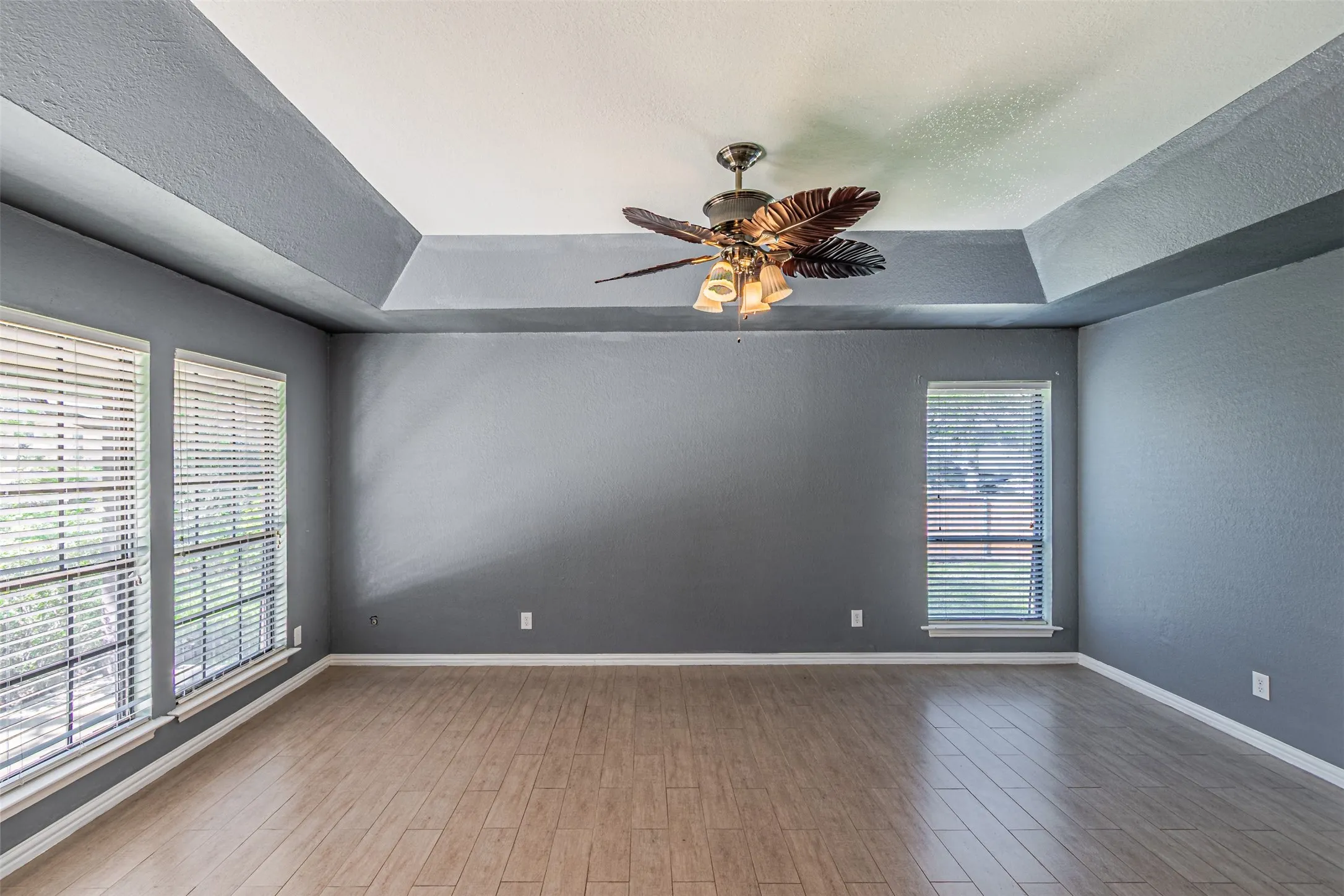 Tray ceiling with a decorative ceiling fan, wood-finish flooring, and multiple windows with blinds
