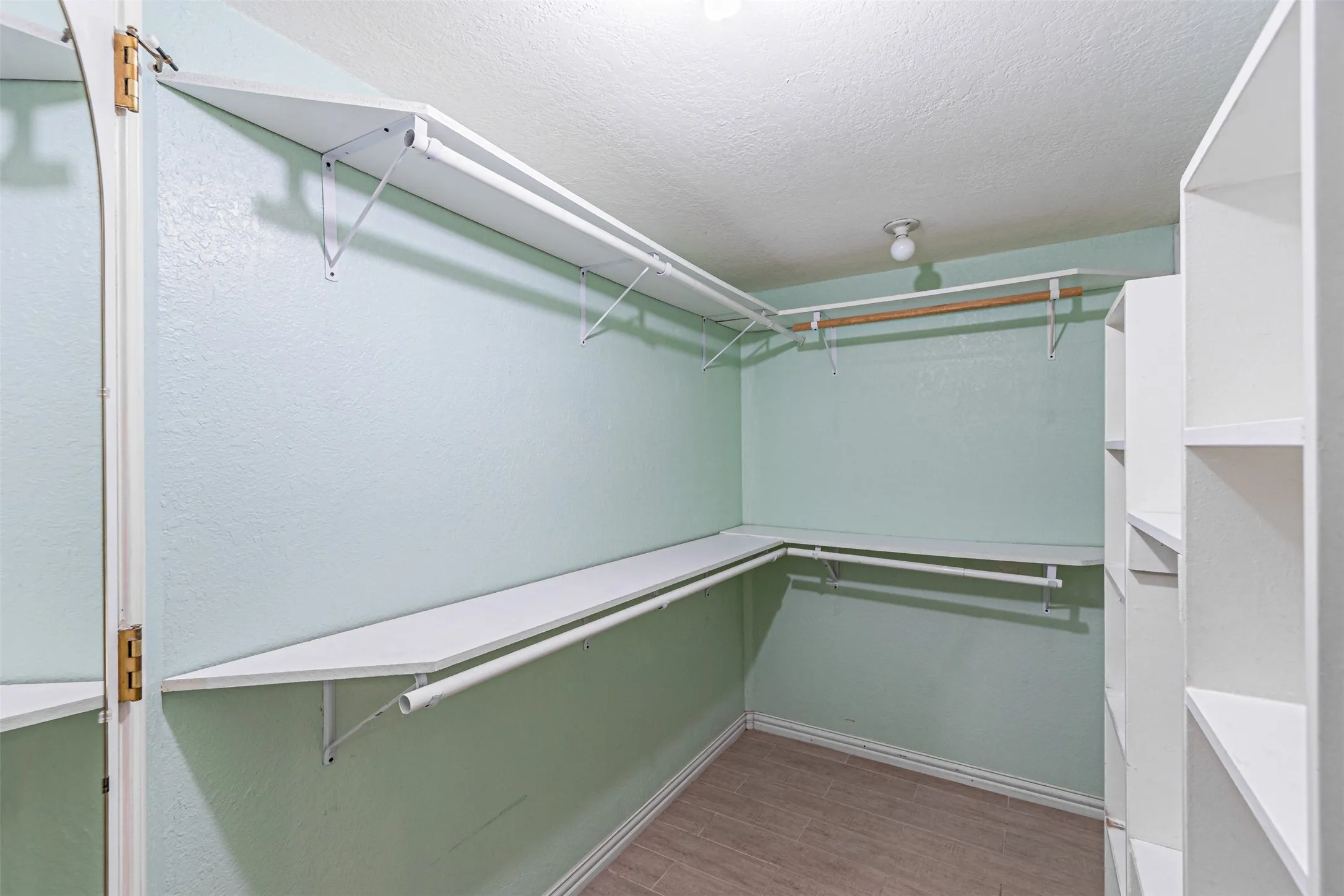 Walk-in closet featuring extensive built-in shelving, multiple hanging rods, and wood-finish flooring