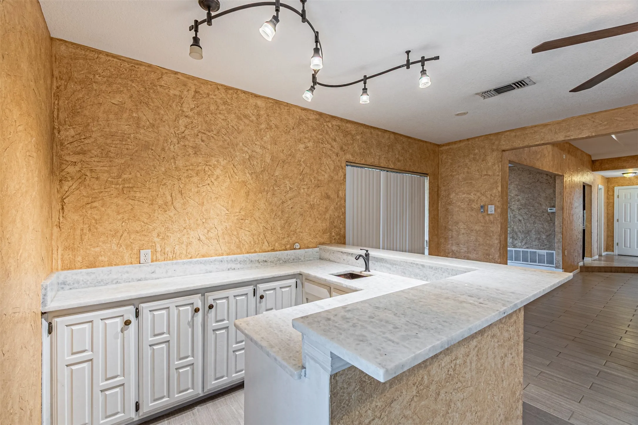 U-shaped counter with a built-in sink, track lighting, white paneled cabinetry, and wood-finish flooring