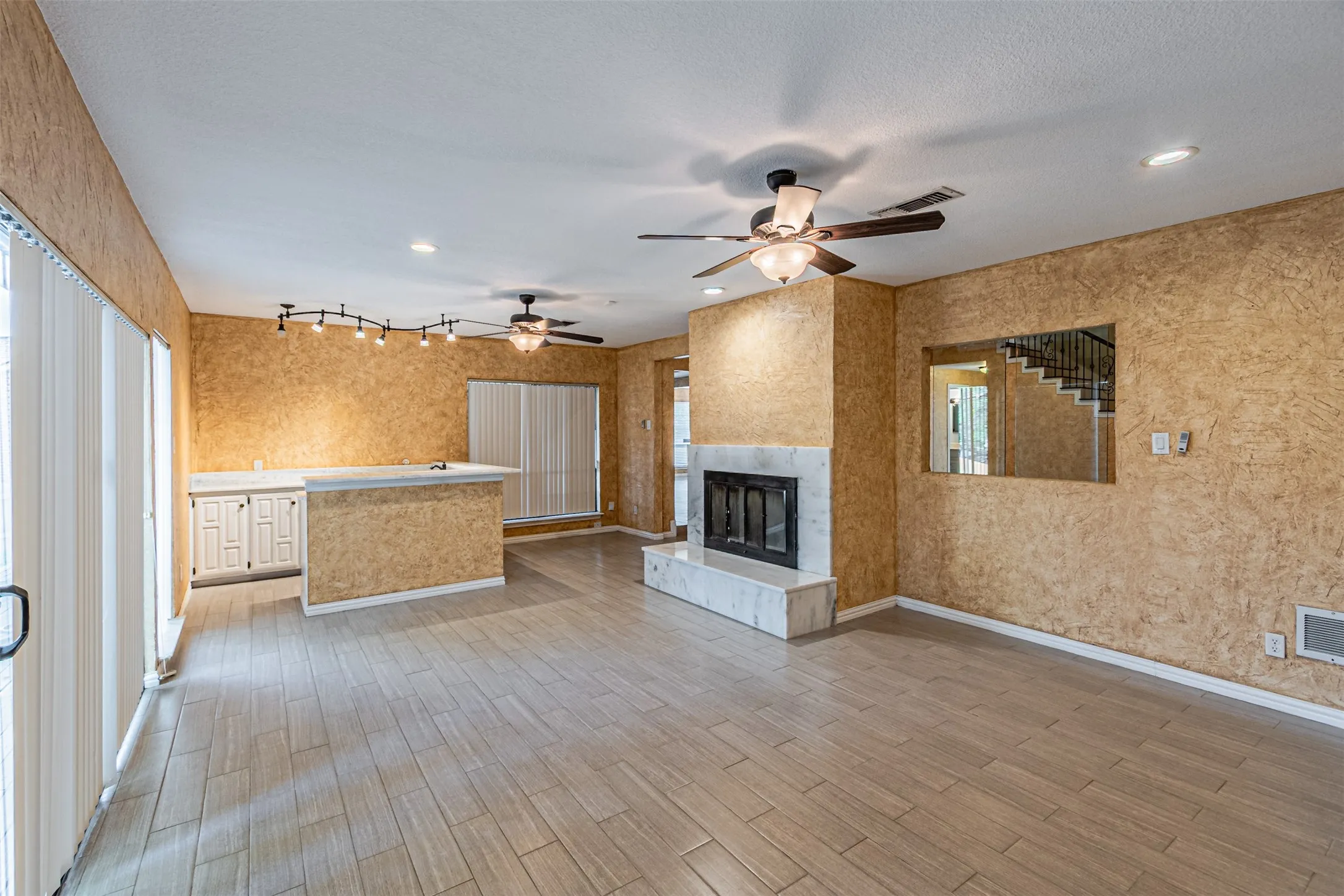 Tile flooring, stone-surround fireplace, built-in cabinetry with light-toned countertop, track lighting, and ceiling fans