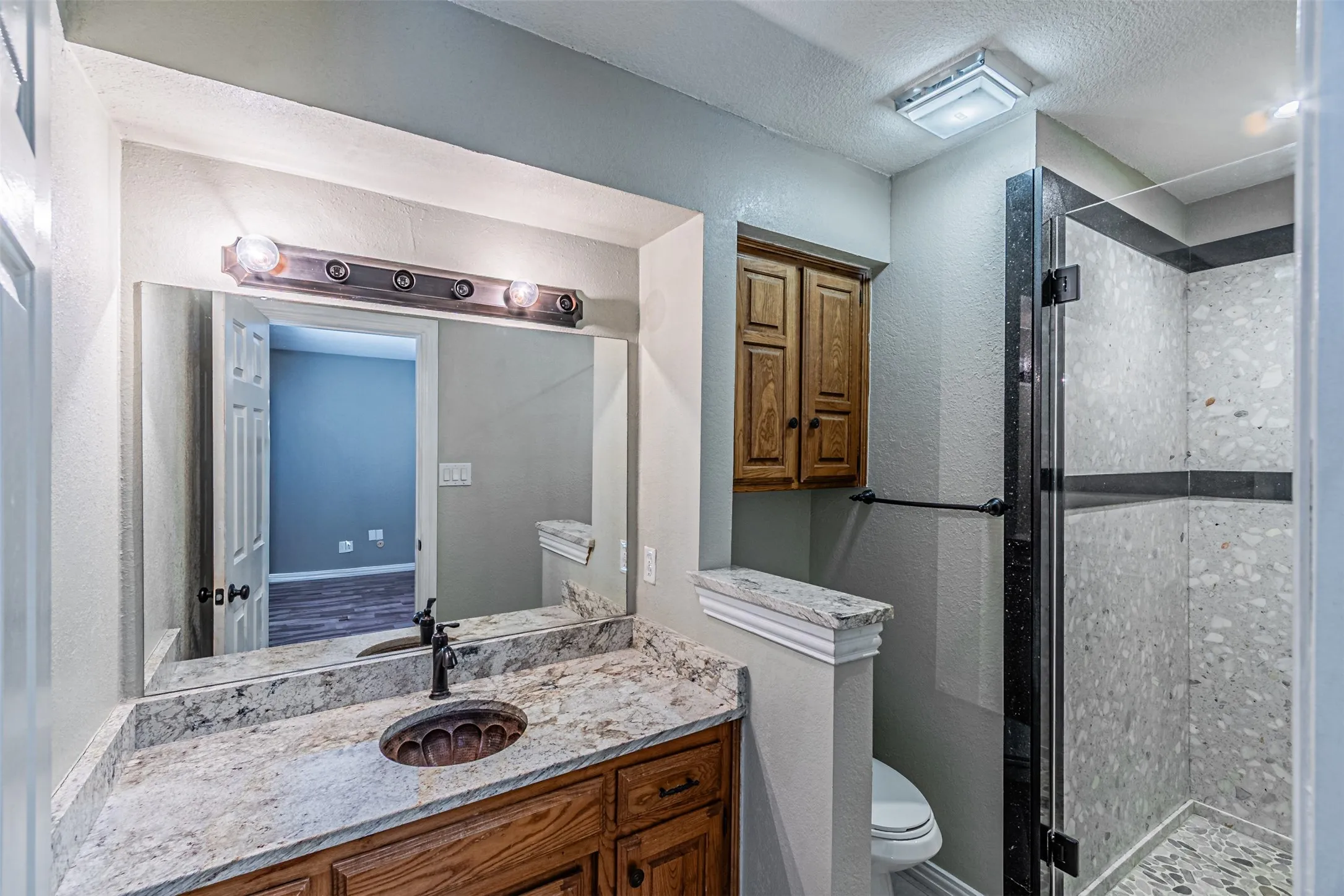 Vanity with an integrated sink, granite-style countertop, wood-finish cabinetry, and a glass-enclosed shower featuring tiled walls