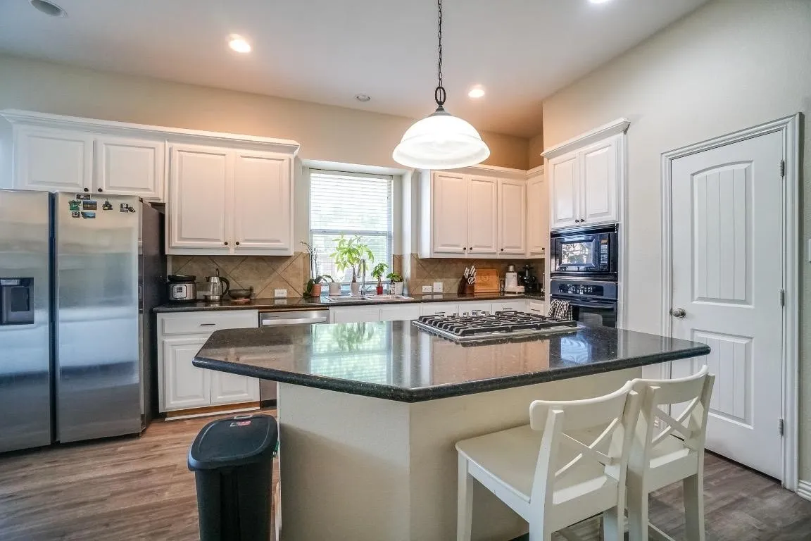 Kitchen featuring a gas range on a central island, white cabinetry, a tile backsplash, and wood-finish flooring