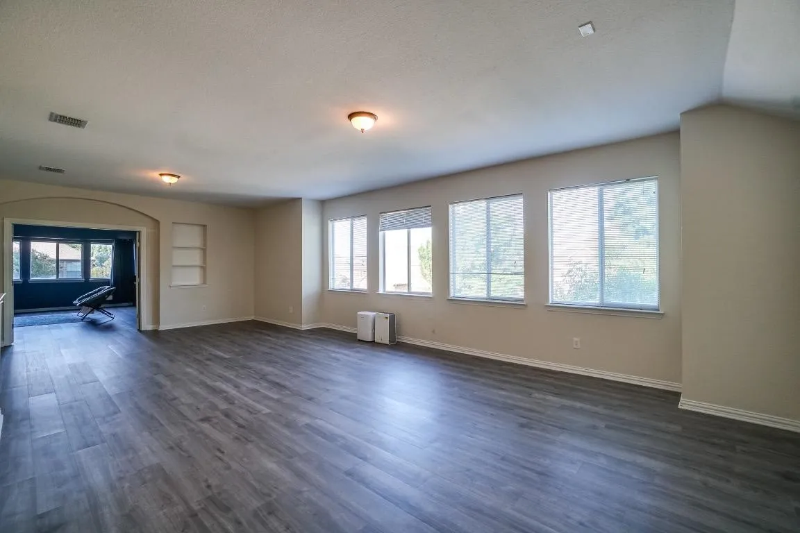 Spacious interior featuring wood-finish flooring, multiple windows with blinds, and recessed shelving