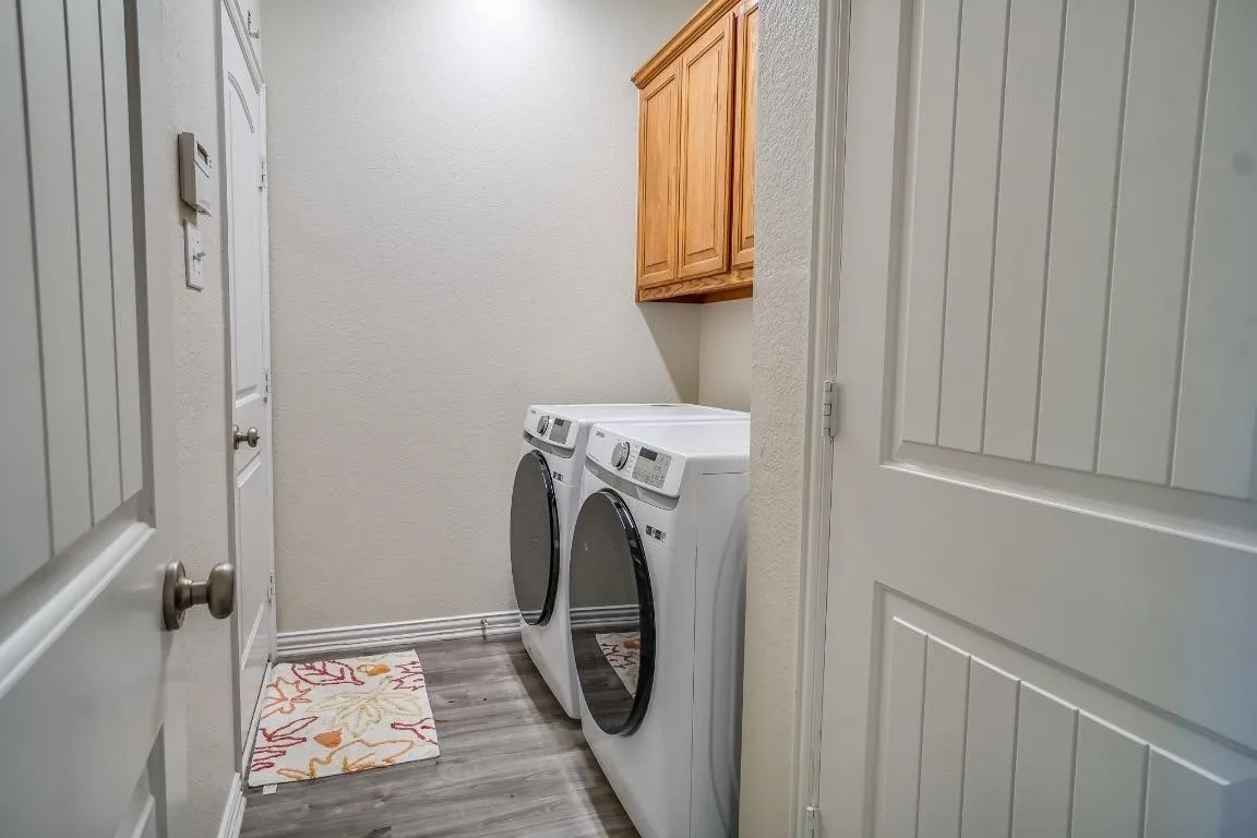 Laundry area featuring wood-finish flooring, overhead cabinetry, and white paneled doors