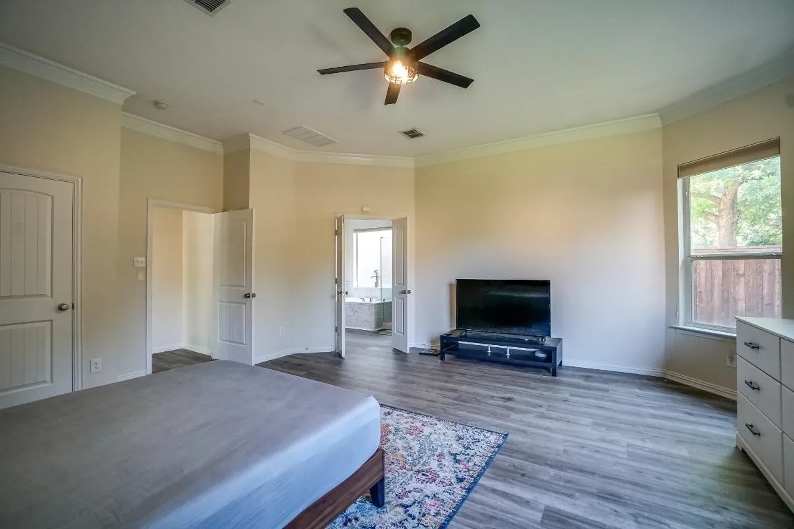 Spacious room featuring wood-finish flooring, a ceiling fan with integrated lighting, and multiple windows
